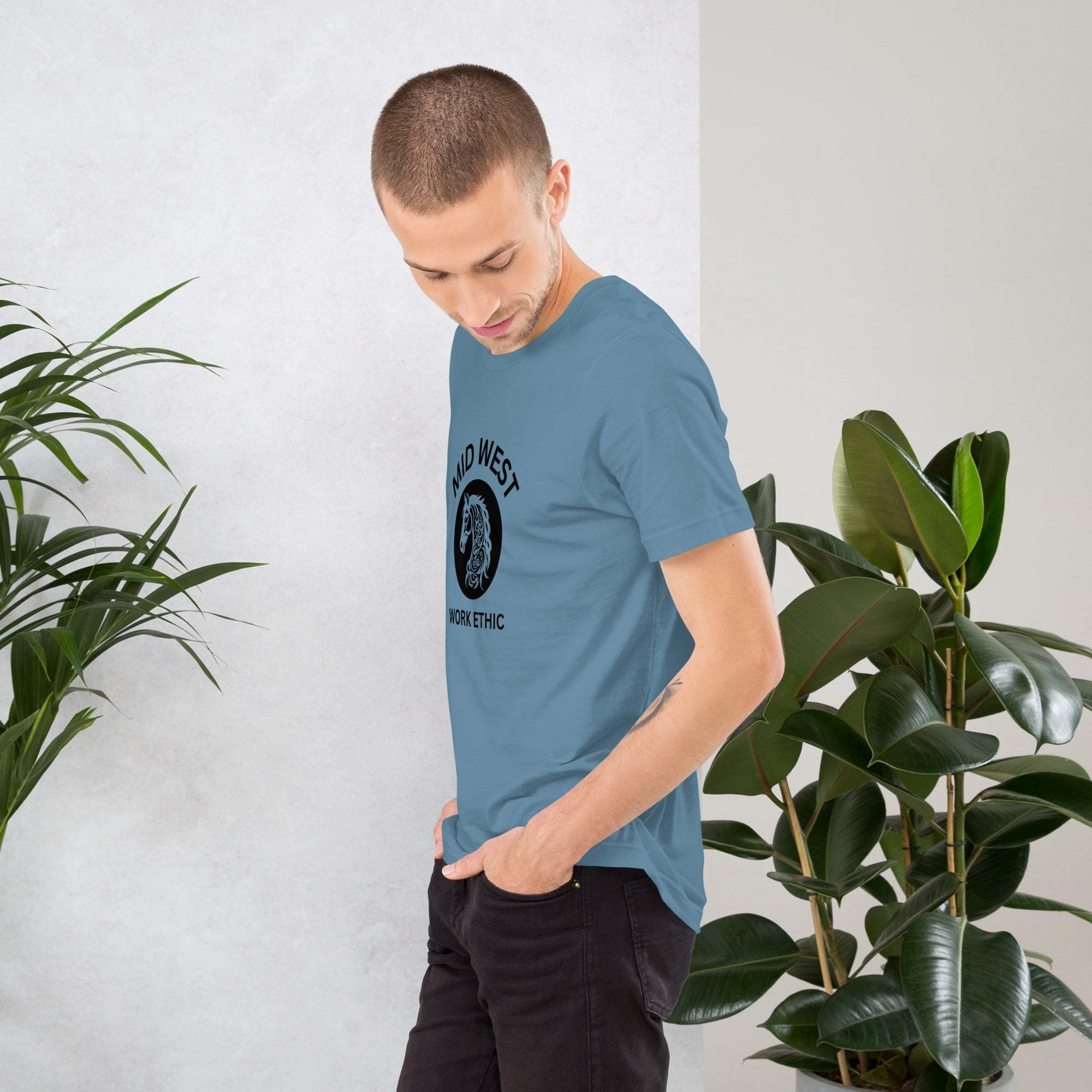 Man wearing blue Midwest Work Ethic T-Shirt with horse graphic standing near plants