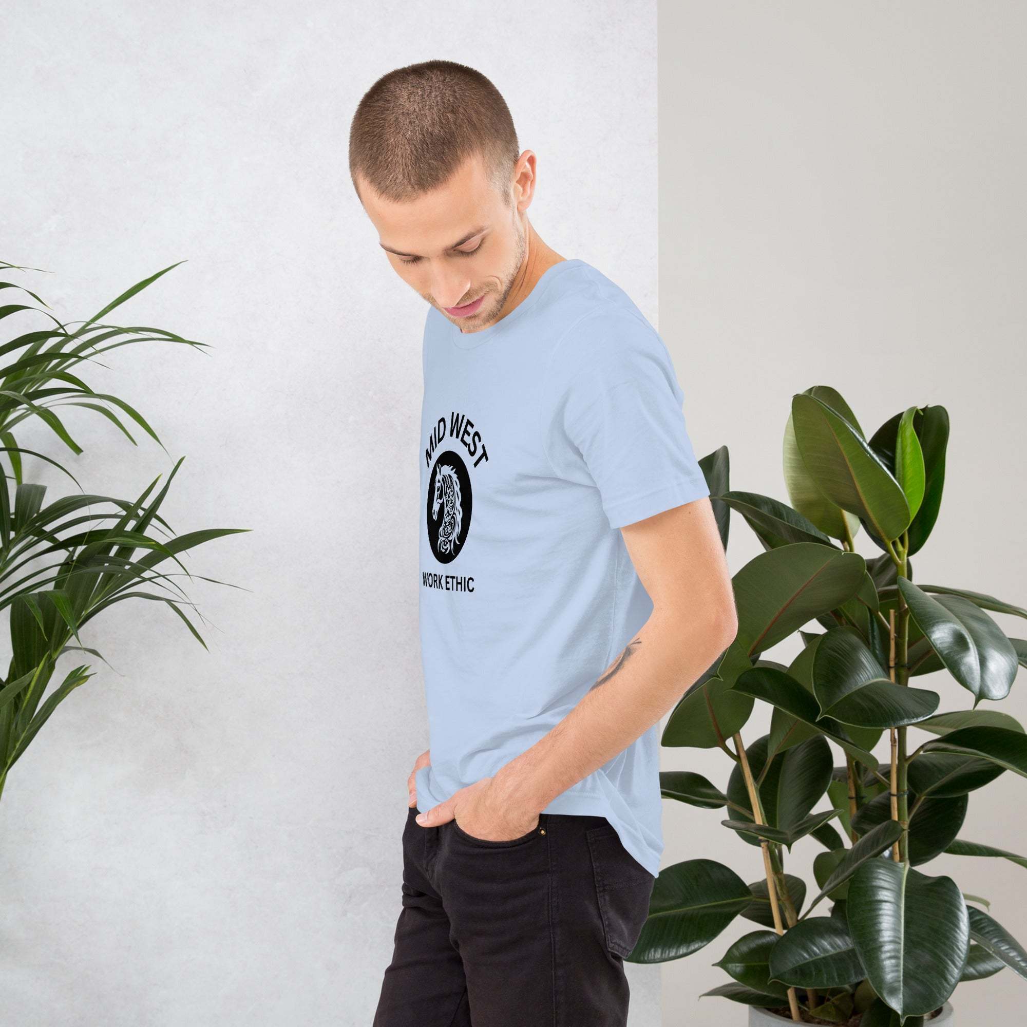 Man wearing light blue Midwest work ethic t-shirt with horse graphic standing near green plants