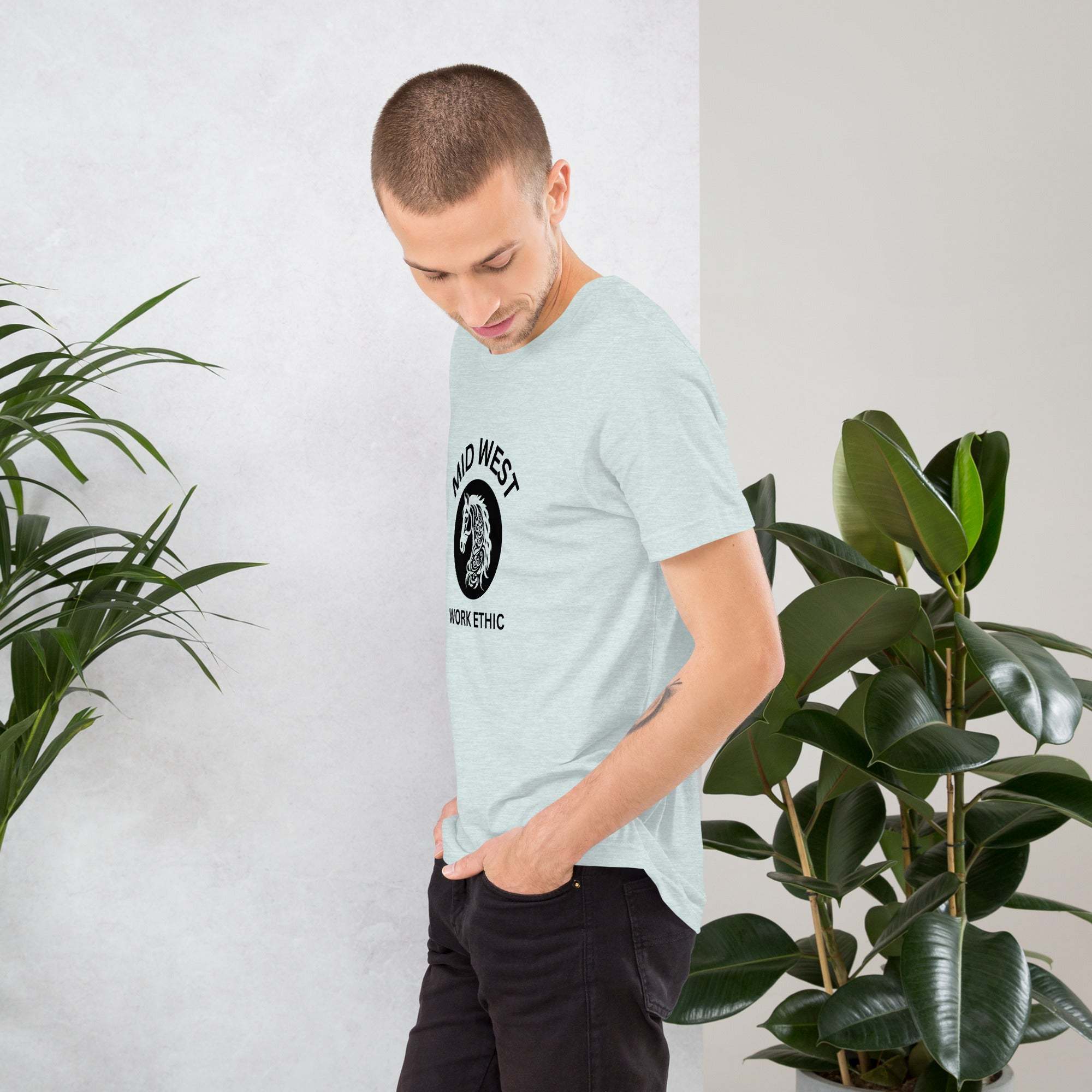Man wearing light gray Midwest T-Shirt with horse graphic and work ethic text standing near green plants