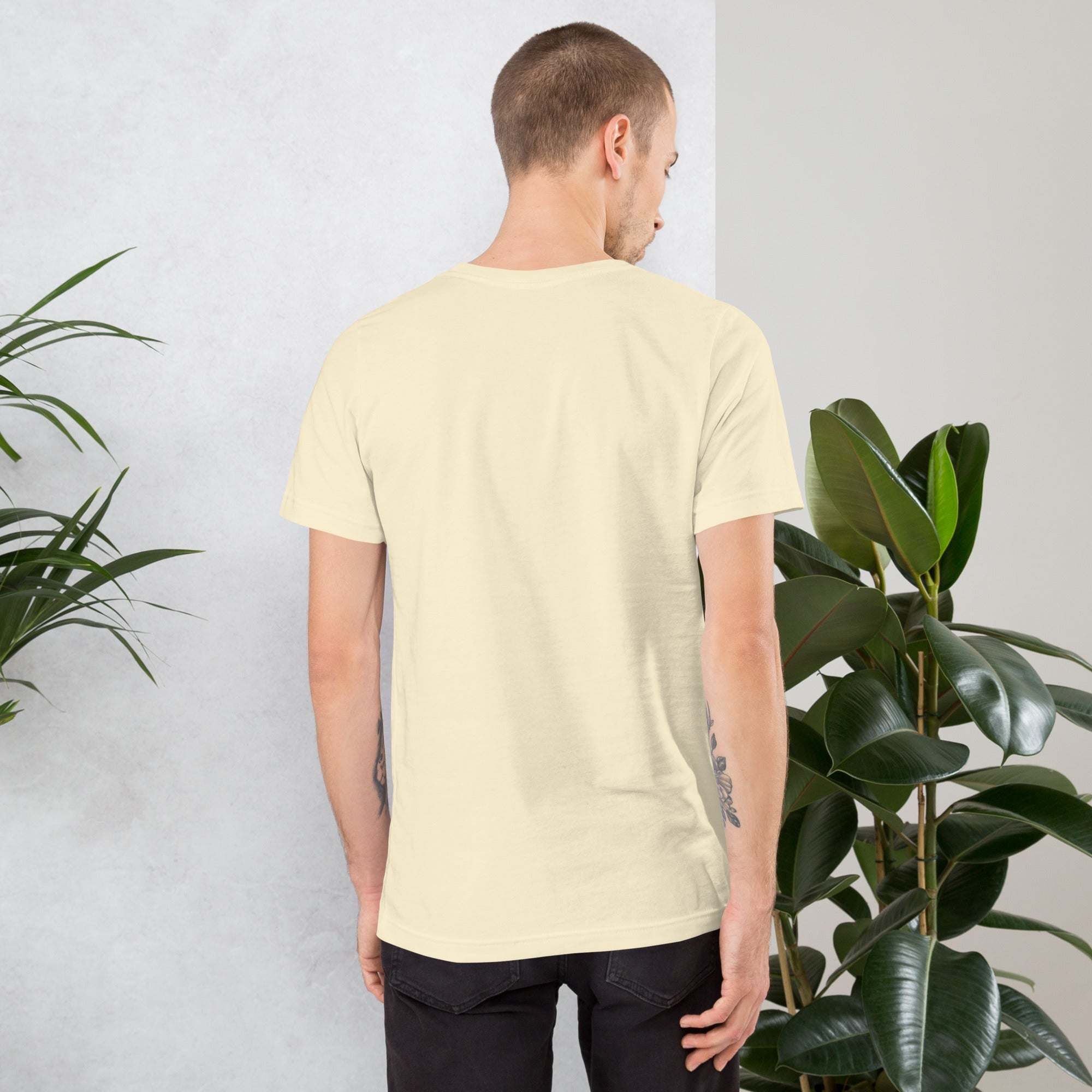 Back view of man wearing cream Midwest T-Shirt standing near green plants indoors