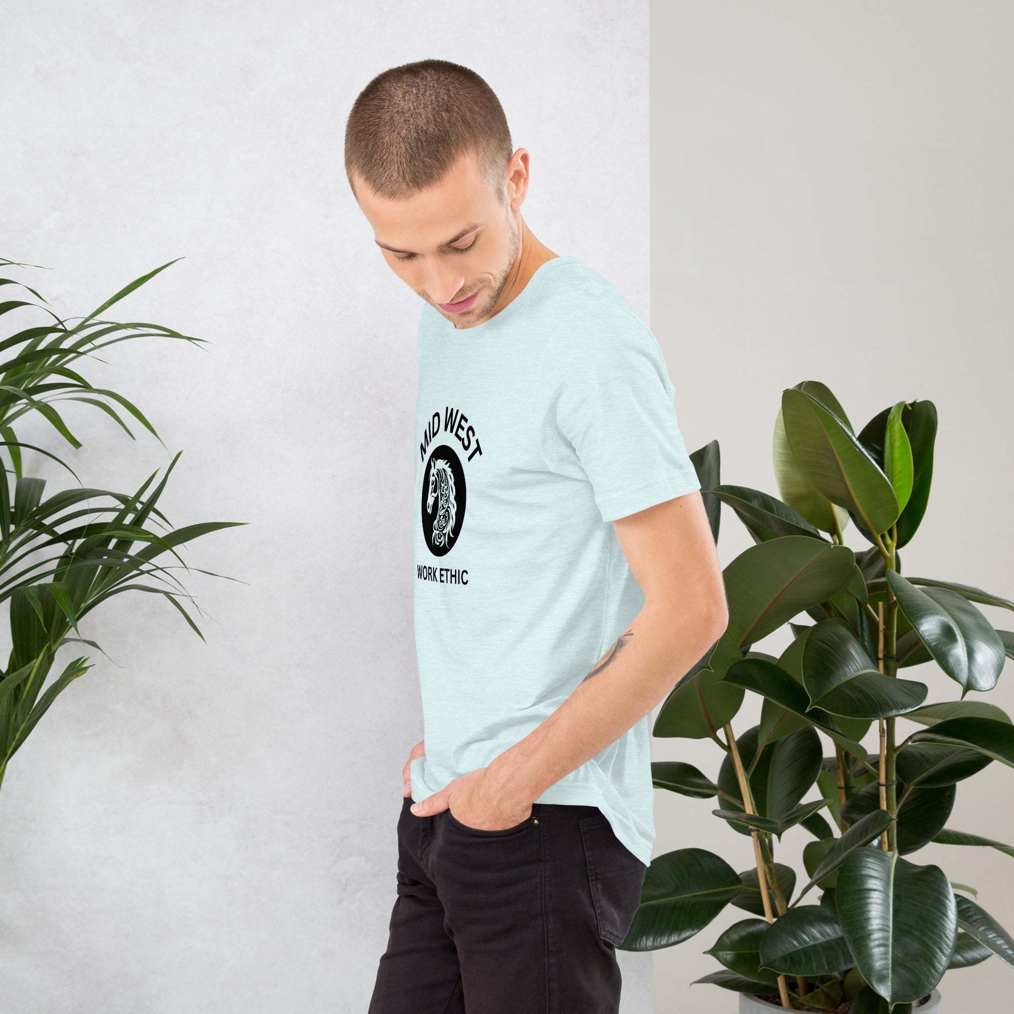 Man wearing light blue Midwest Work Ethic T-Shirt with horse graphic standing indoors next to green plants