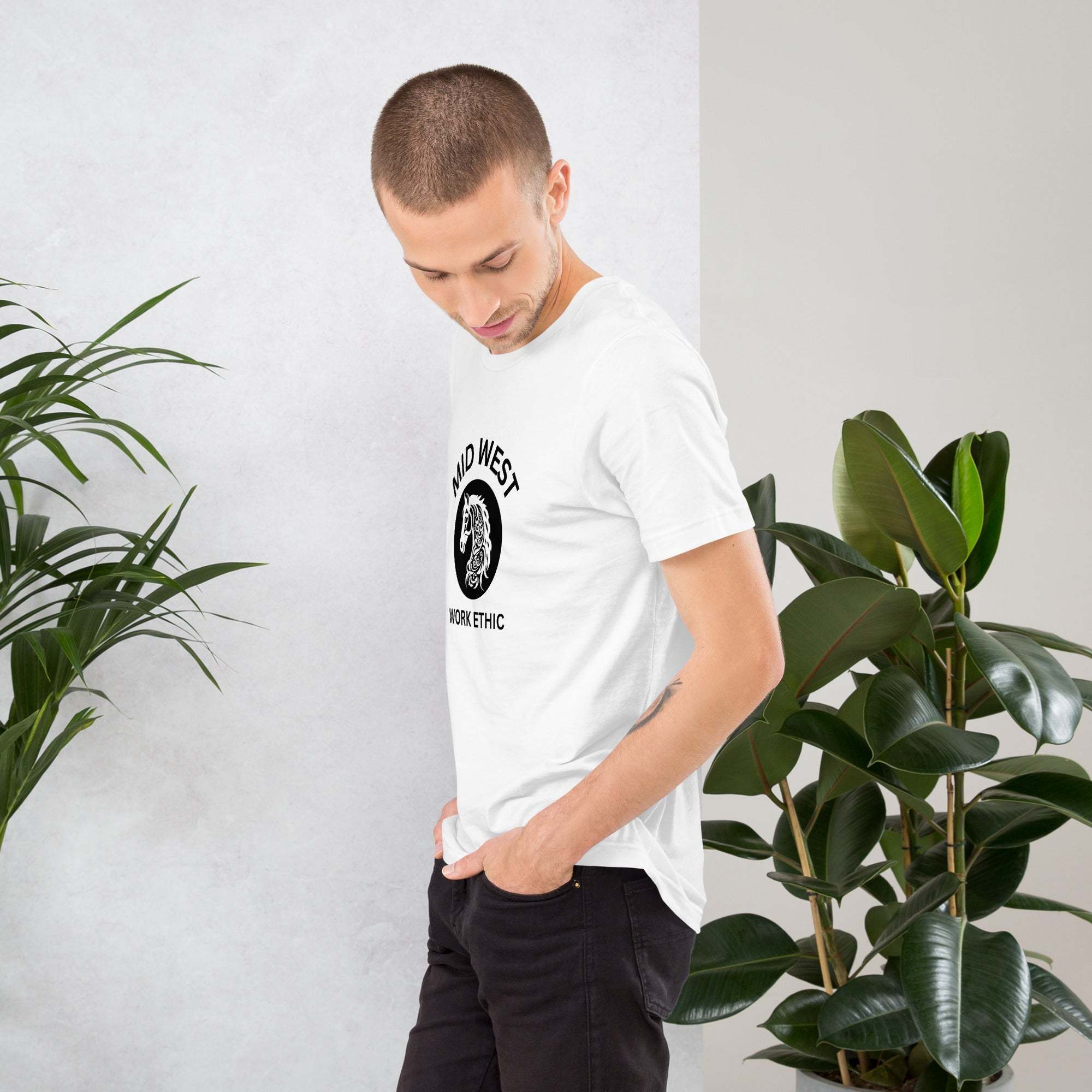 Man wearing white Midwest T-Shirt with black horse graphic and work ethic text standing near plants