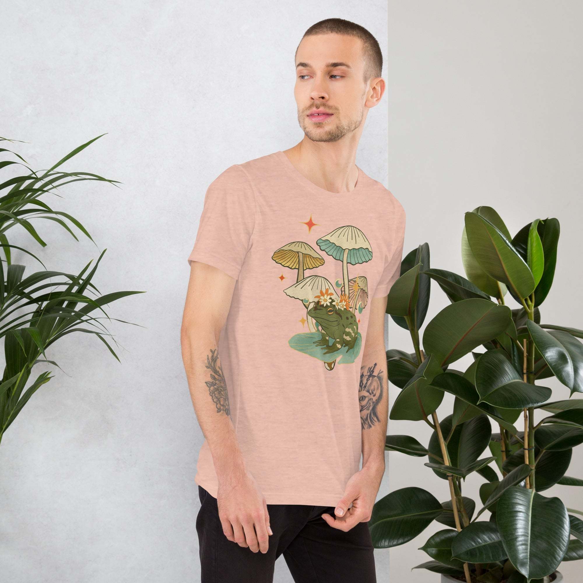 Man wearing vintage aesthetic frog and mushroom graphic t-shirt in soft cotton next to green plants