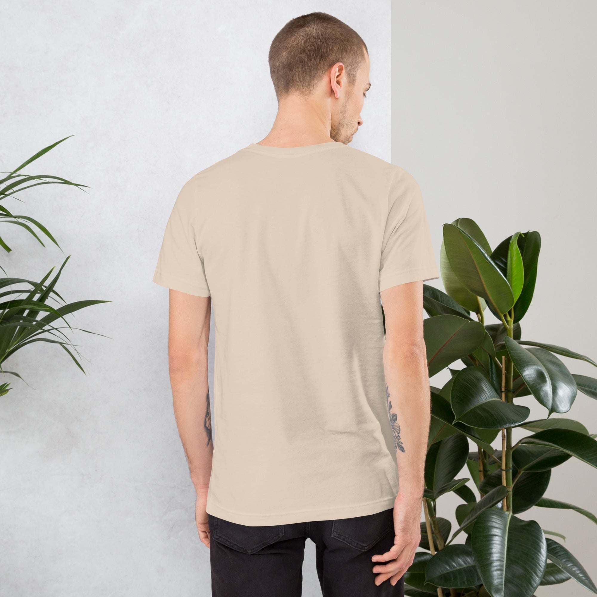 Back view of man wearing beige vintage aesthetic frog and mushroom graphic T-shirt in casual indoor setting