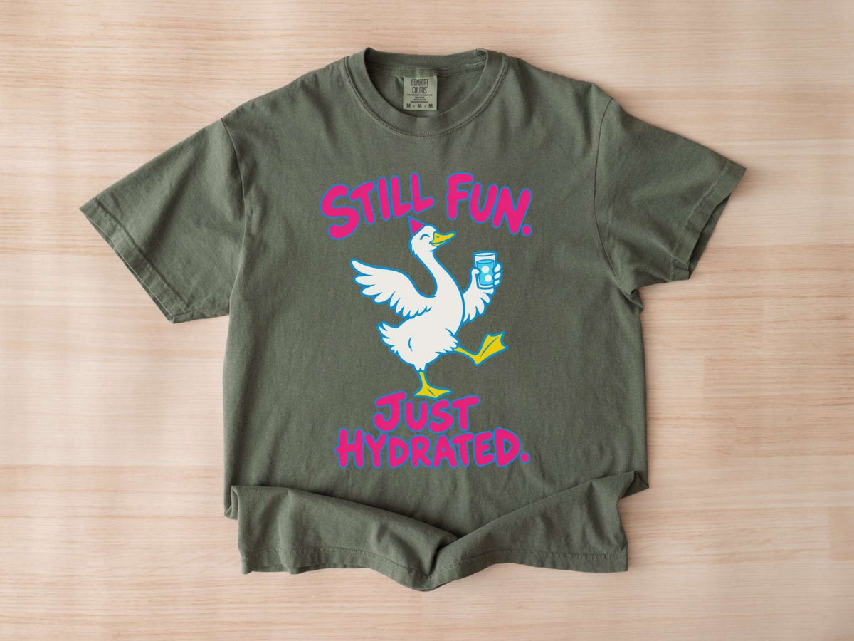 A moss green Comfort Colors crewneck t-shirt featuring a graphic of a white goose holding a blue water bottle, with the pink text 'STILL FUN. JUST HYDRATED.