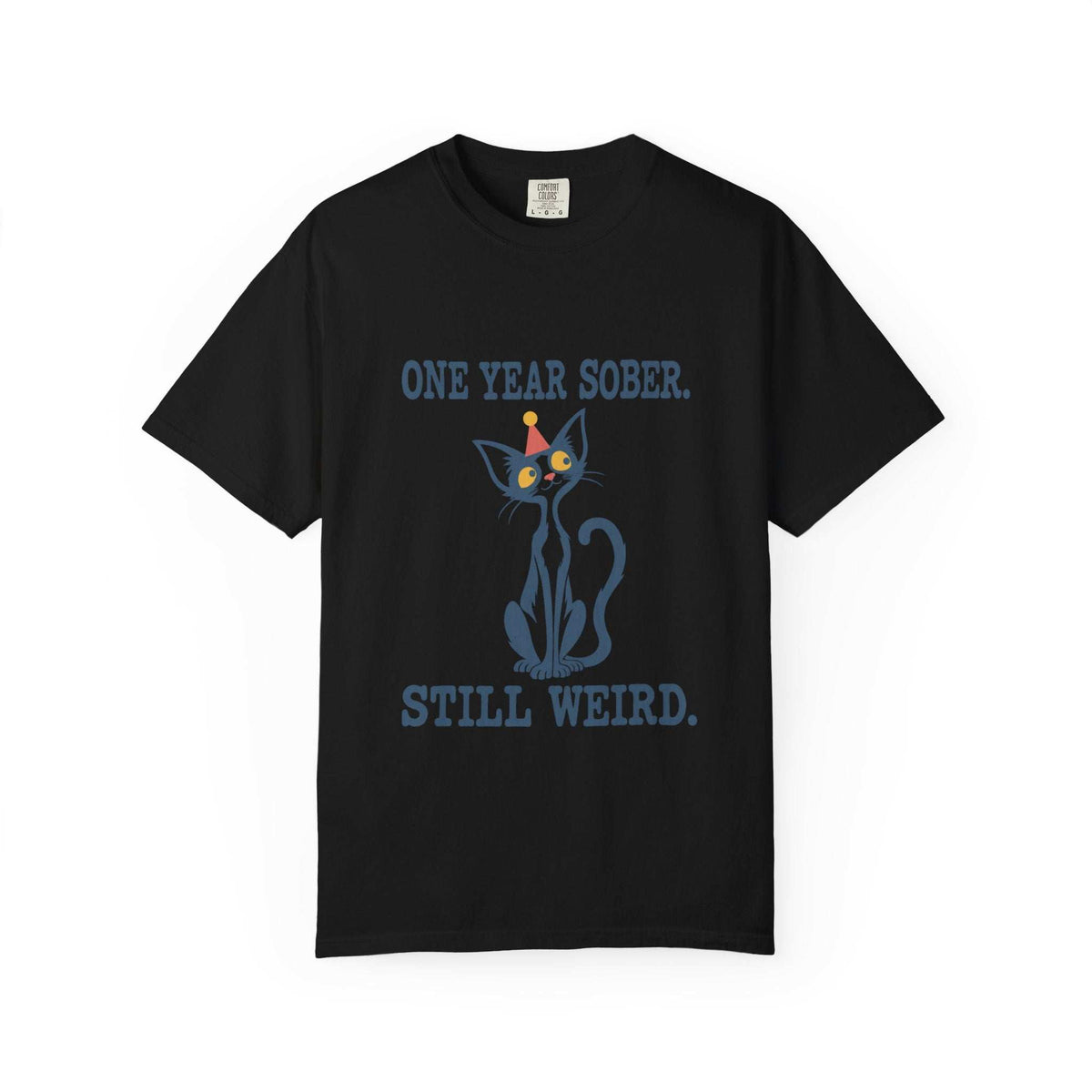 Flat lay of a black Comfort Colors 1717 t-shirt featuring a navy cat in a red party hat and “One Year Sober. Still Weird.” lettering.