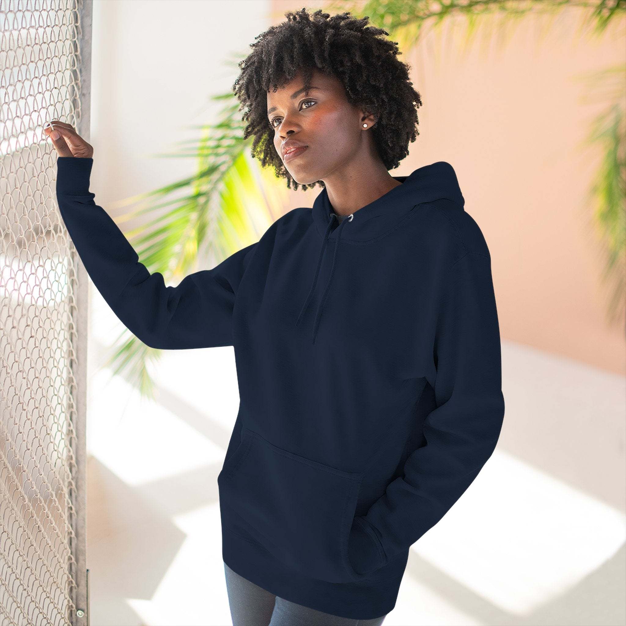 Woman wearing navy blue fleece hoodie with kangaroo pocket and hood indoors with sunlight and plants in background