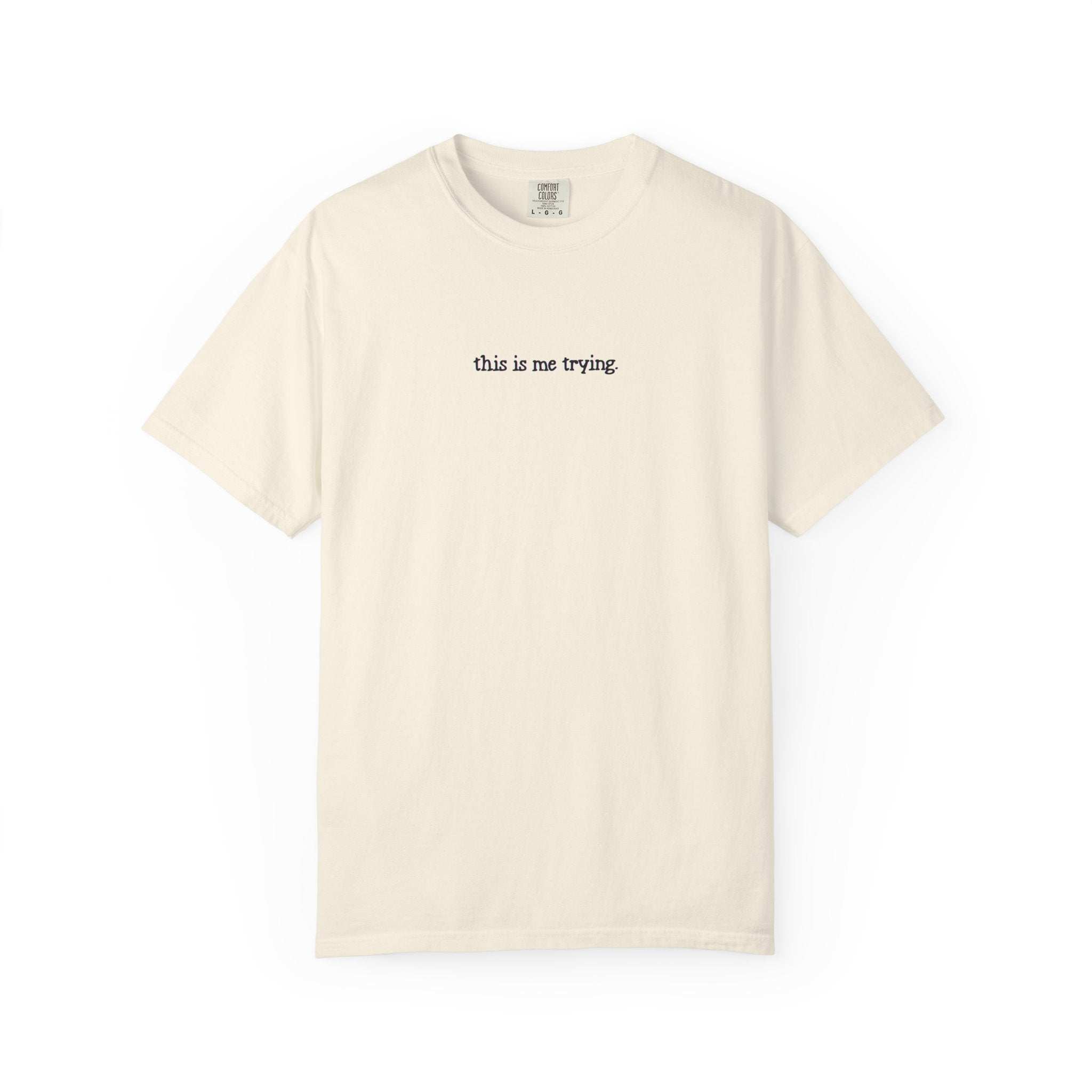 Beige t-shirt with 'this is me trying' text on a white background