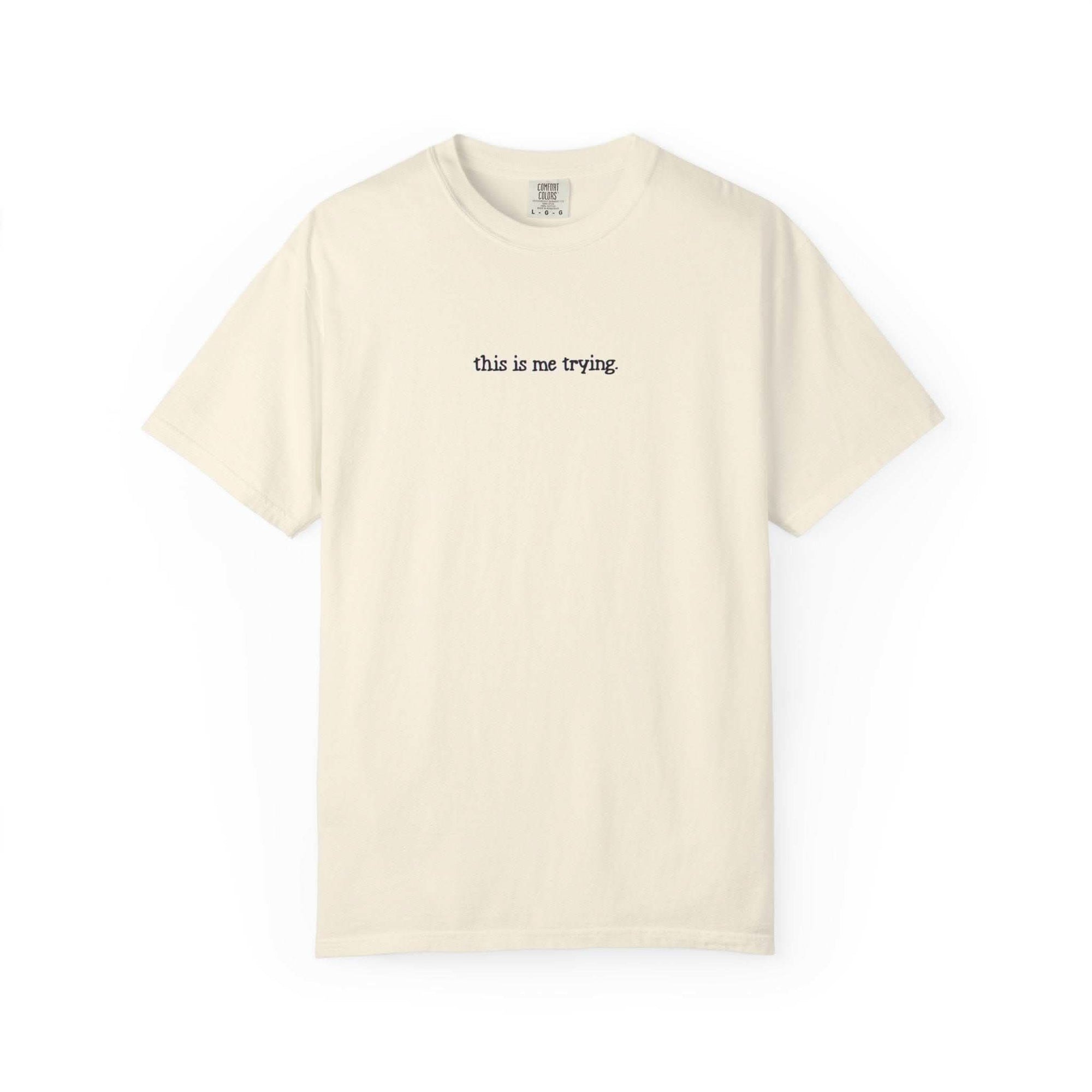Beige t-shirt with 'this is me trying' text on a white background