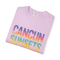 Folded pink t-shirt with 'Cancun Sunsets' text in rainbow colors on a white background