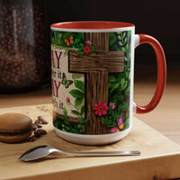 Mug with cross design and floral elements on a wooden surface with coffee beans and a macaron.