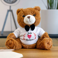 Seated light-brown teddy bear wearing a white T-shirt with personalized heart names and black bow tie, perfect Valentine's gift