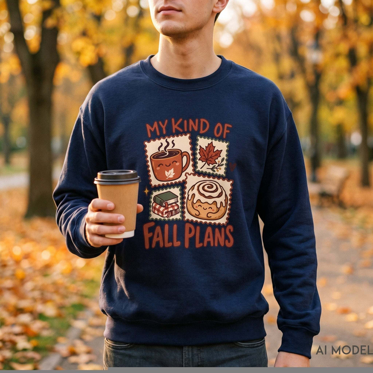 Man wearing a navy My Kind of Fall Plans crewneck sweatshirt with autumn stamp graphics, holding a takeaway coffee among golden fall leaves.