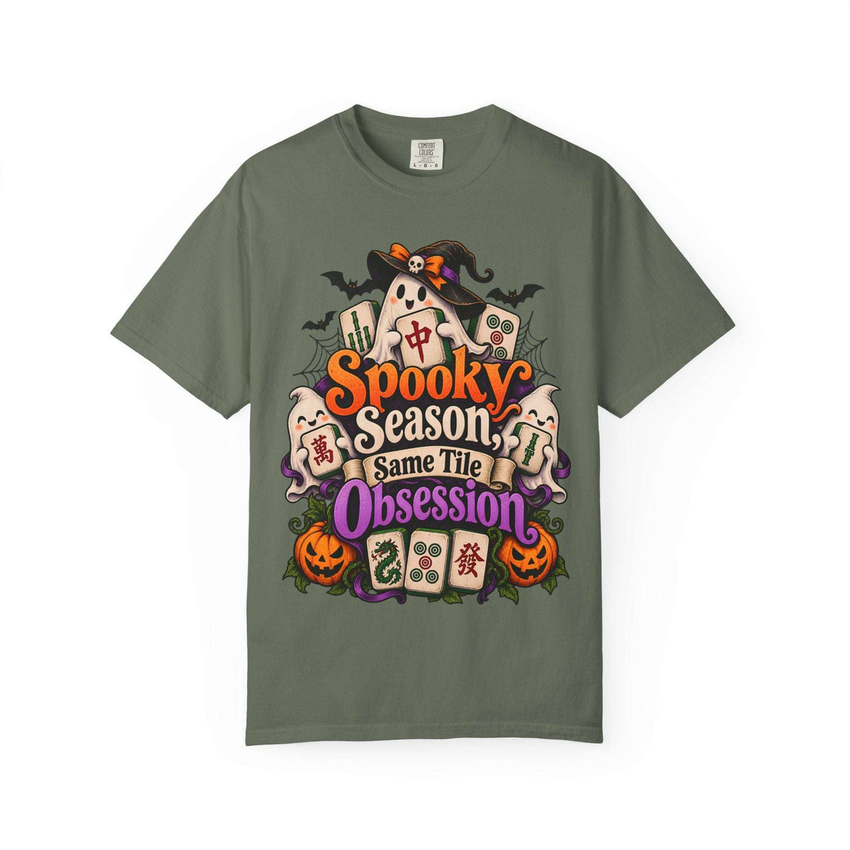 Flat lay of a moss green Halloween mahjong T-shirt with ghosts, pumpkins, mahjong tiles and “Spooky Season, Same Tile Obsession” lettering.