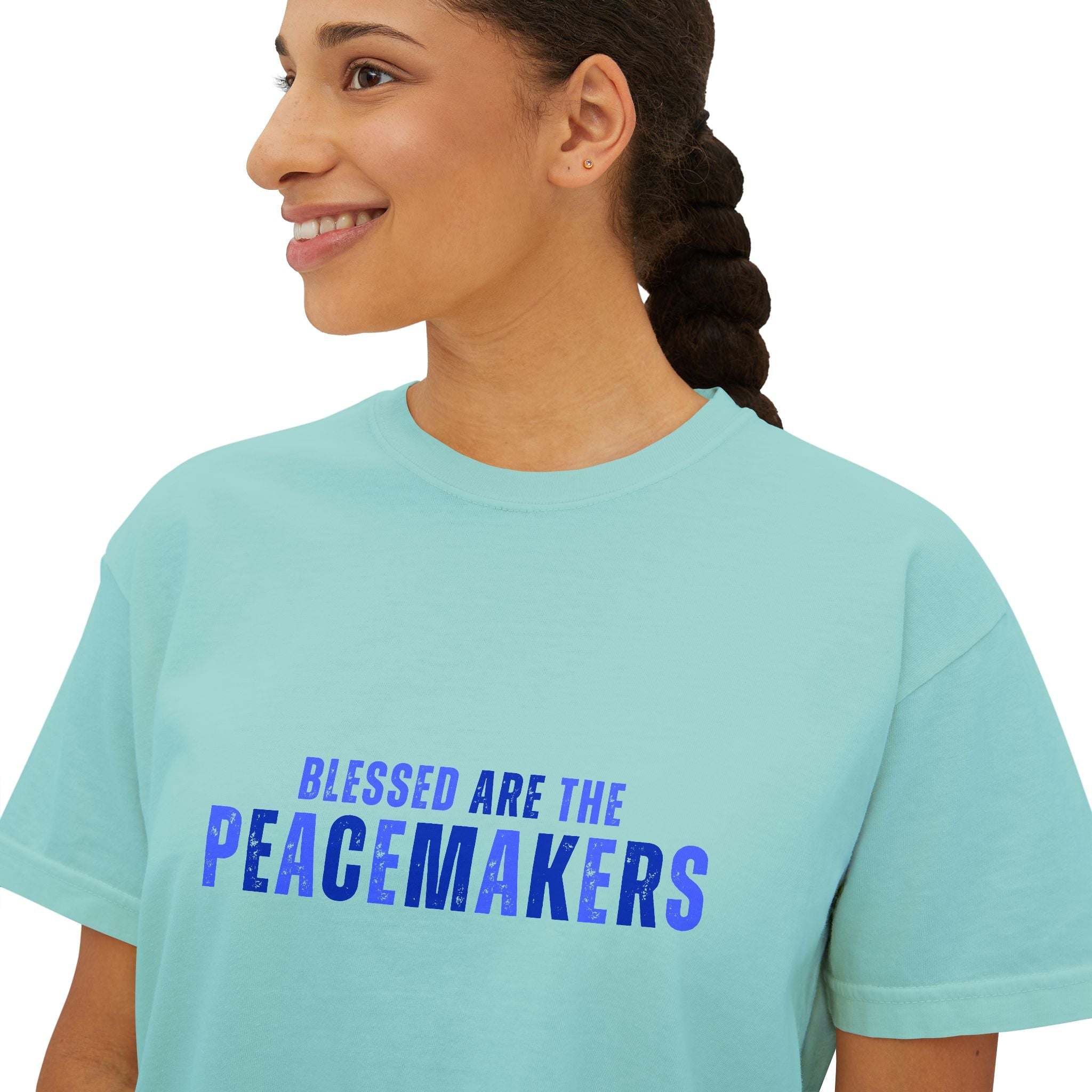 Woman wearing a light blue tee blessed be the peacemakers boxy shirt with blue text promoting peace and unity