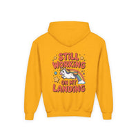 Kids hoodie with colorful unicorn rainbow design and playful "Still Working On My Landing" text