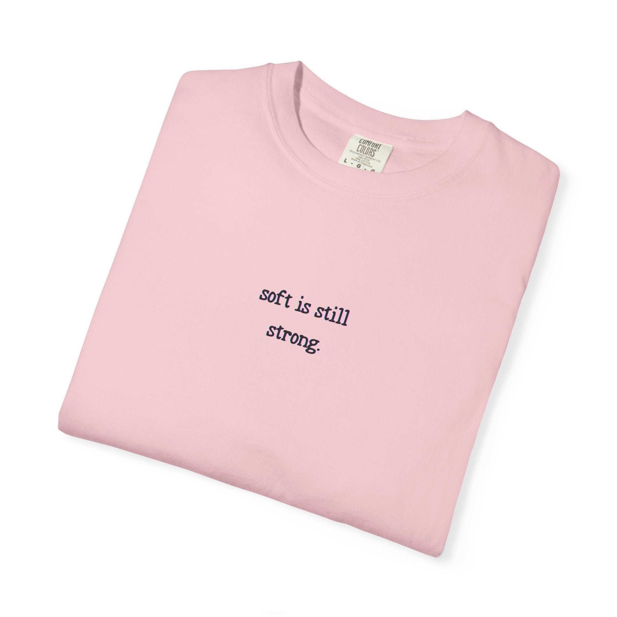 Folded pink t-shirt with 'soft is still strong' text on a white background