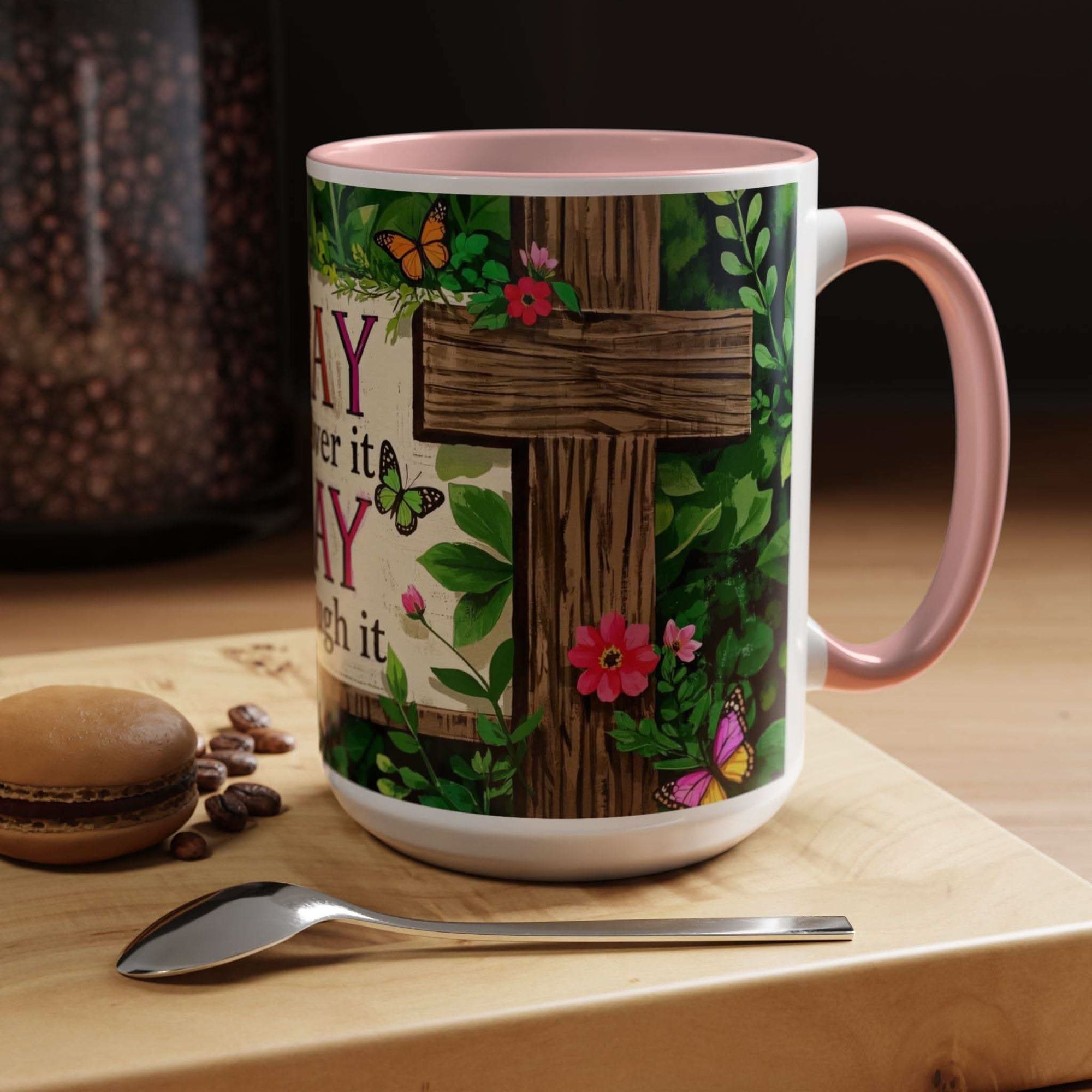 Mug with floral and cross design on a wooden surface with coffee beans and a macaron.