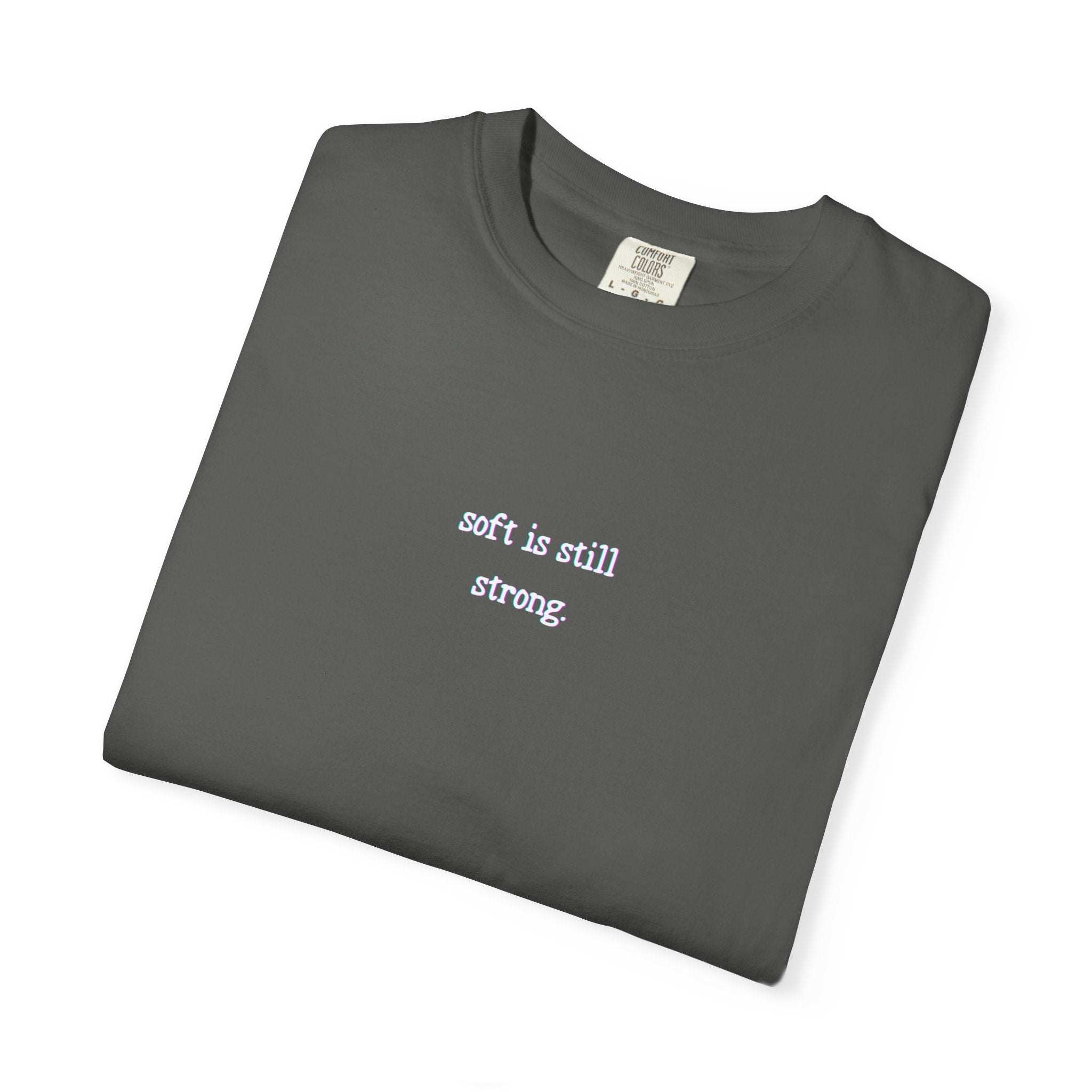 Folded dark gray t-shirt with 'soft is still strong' text on a white background
