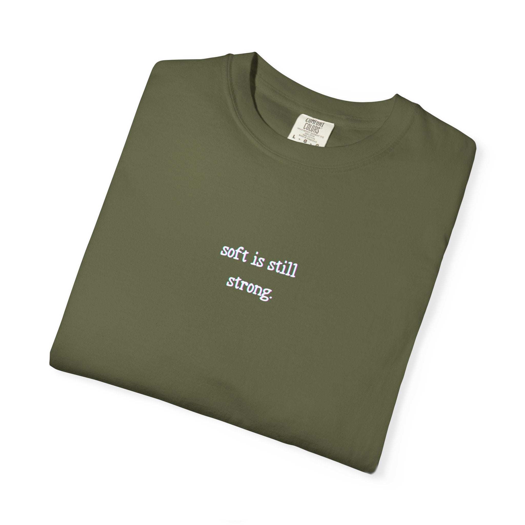 Folded green t-shirt with 'soft is still strong' text on a white background