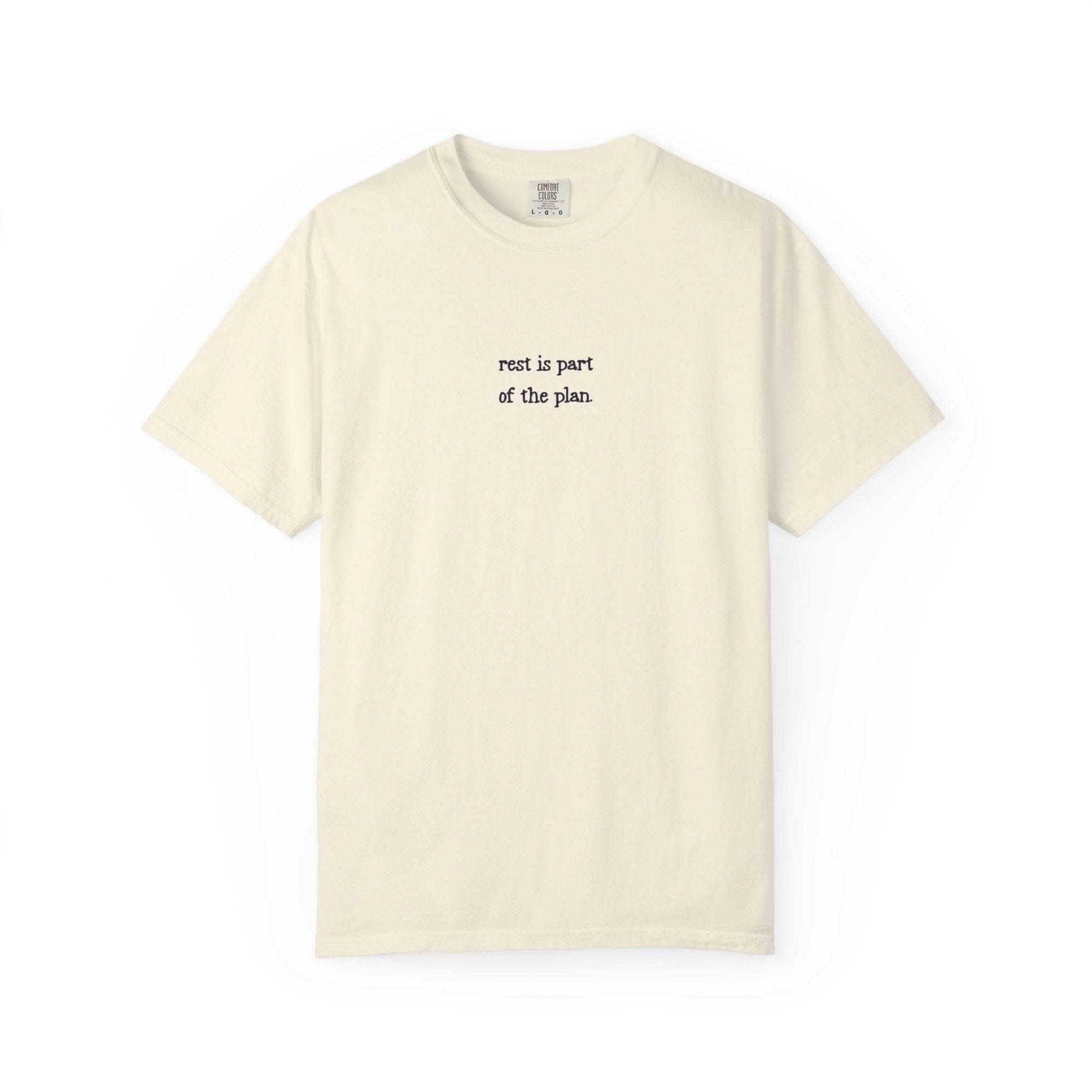 Beige t-shirt with text 'rest is part of the plan' on a white background