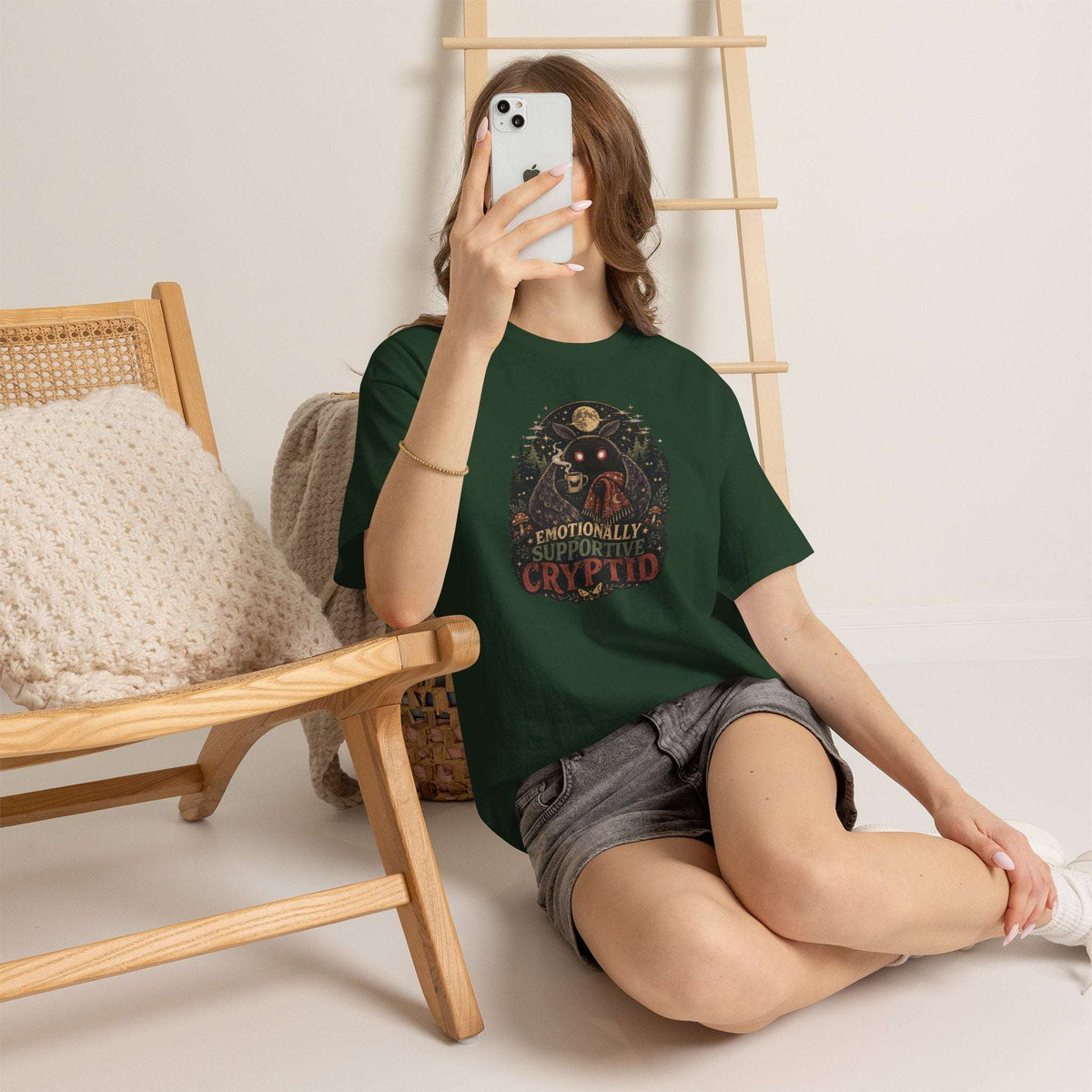 Surreal Mothman cryptid tee with glowing eyes, cozy blanket, and coffee mug under moonlit forest canopy on soft cotton shirt