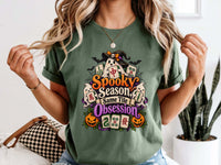 Model wearing a moss green Halloween mahjong T-shirt with ghosts, pumpkins, mahjong tiles and “Spooky Season, Same Tile Obsession” lettering.
