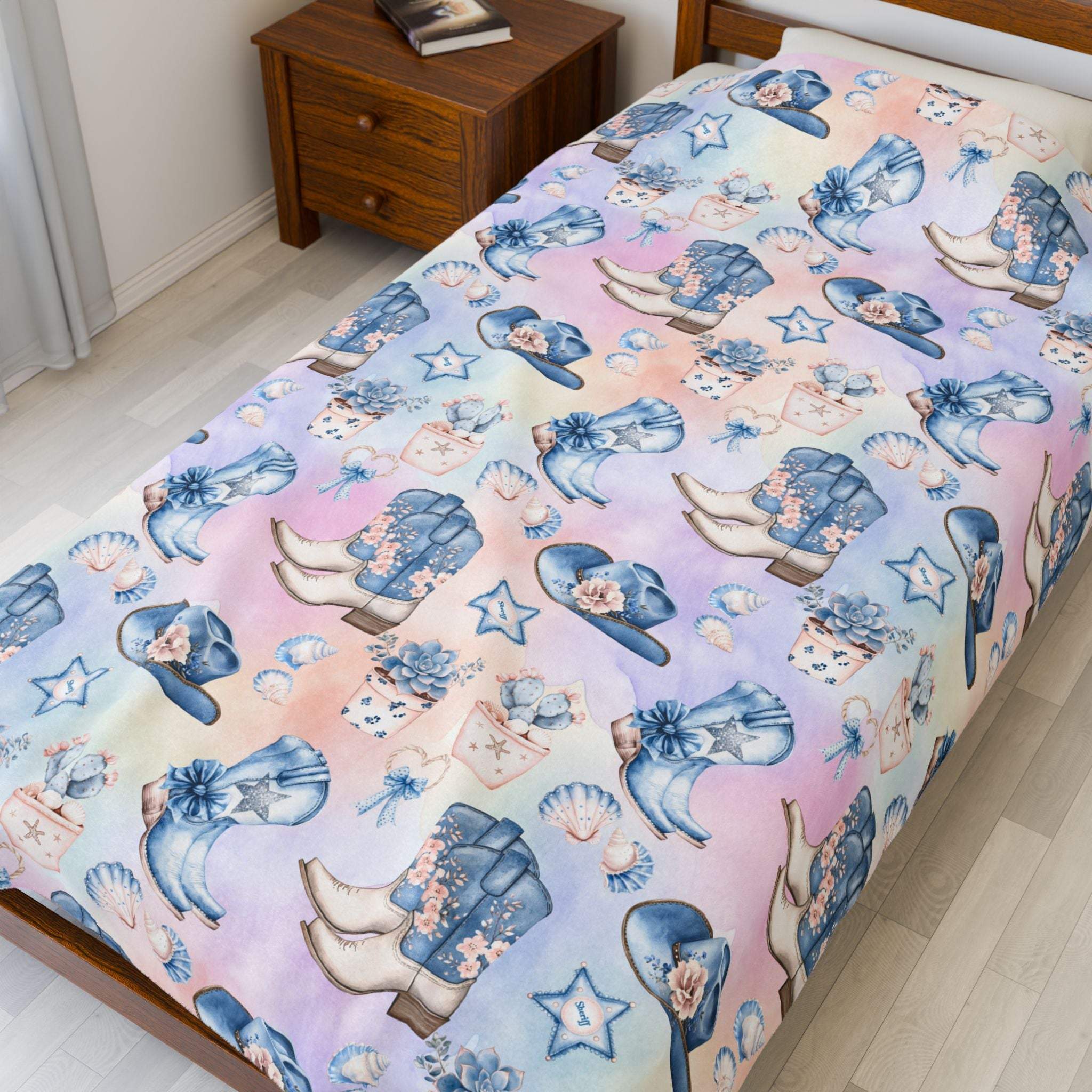 Coastal Cowgirl design plush blanket with boots, hats, and stars on pastel background on bed