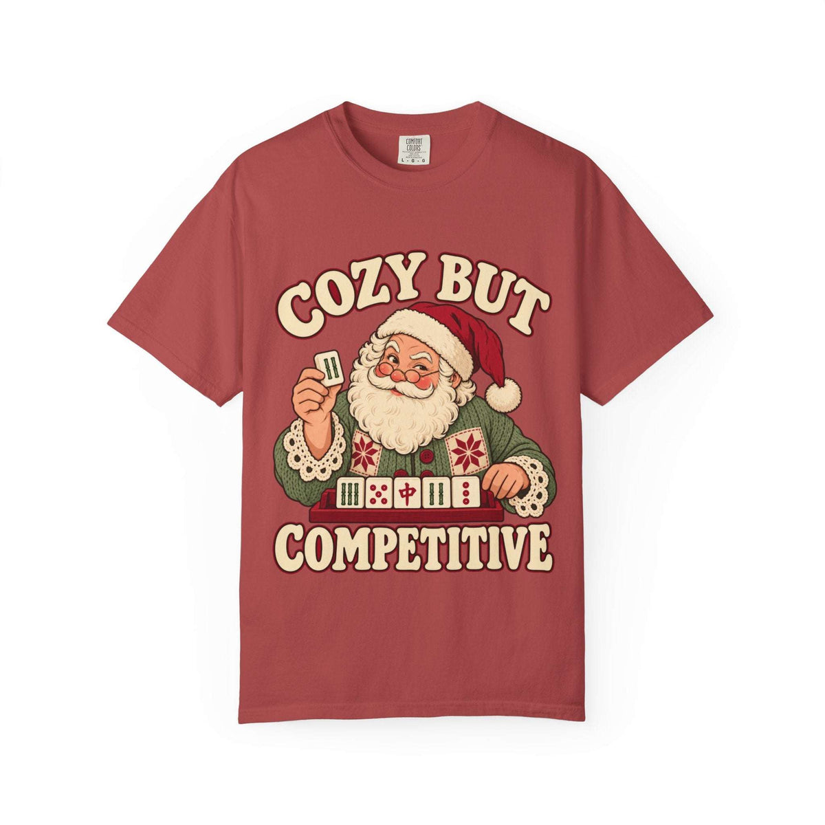 Flat lay of a Crimson red Comfort Colors T-shirt with Santa holding a mahjong tile above a tile rack and cream “Cozy But Competitive” lettering.