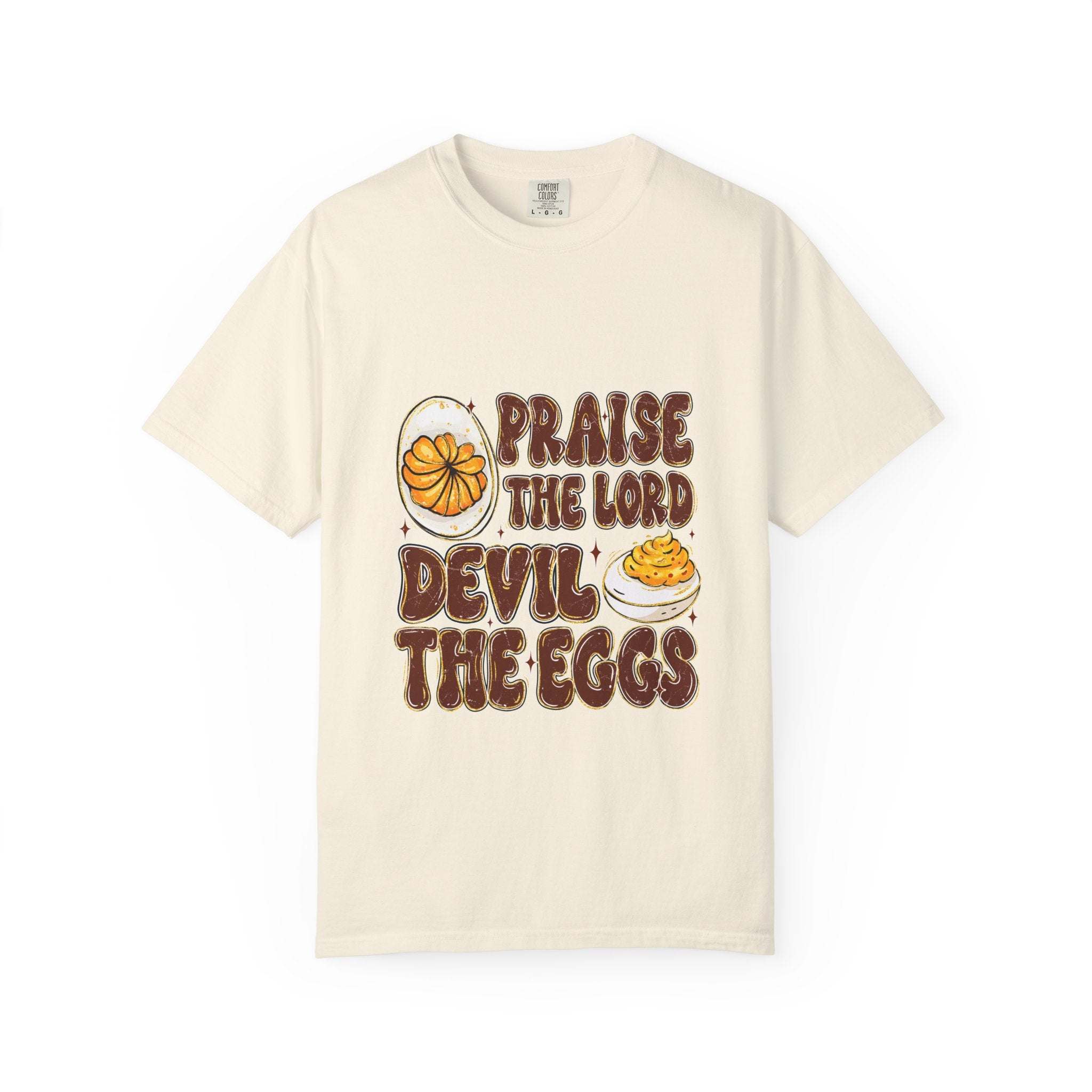 White Christian-themed t-shirt featuring 'Praise the Lord, Devil the Eggs' text design, available in sizes S, M, and L.