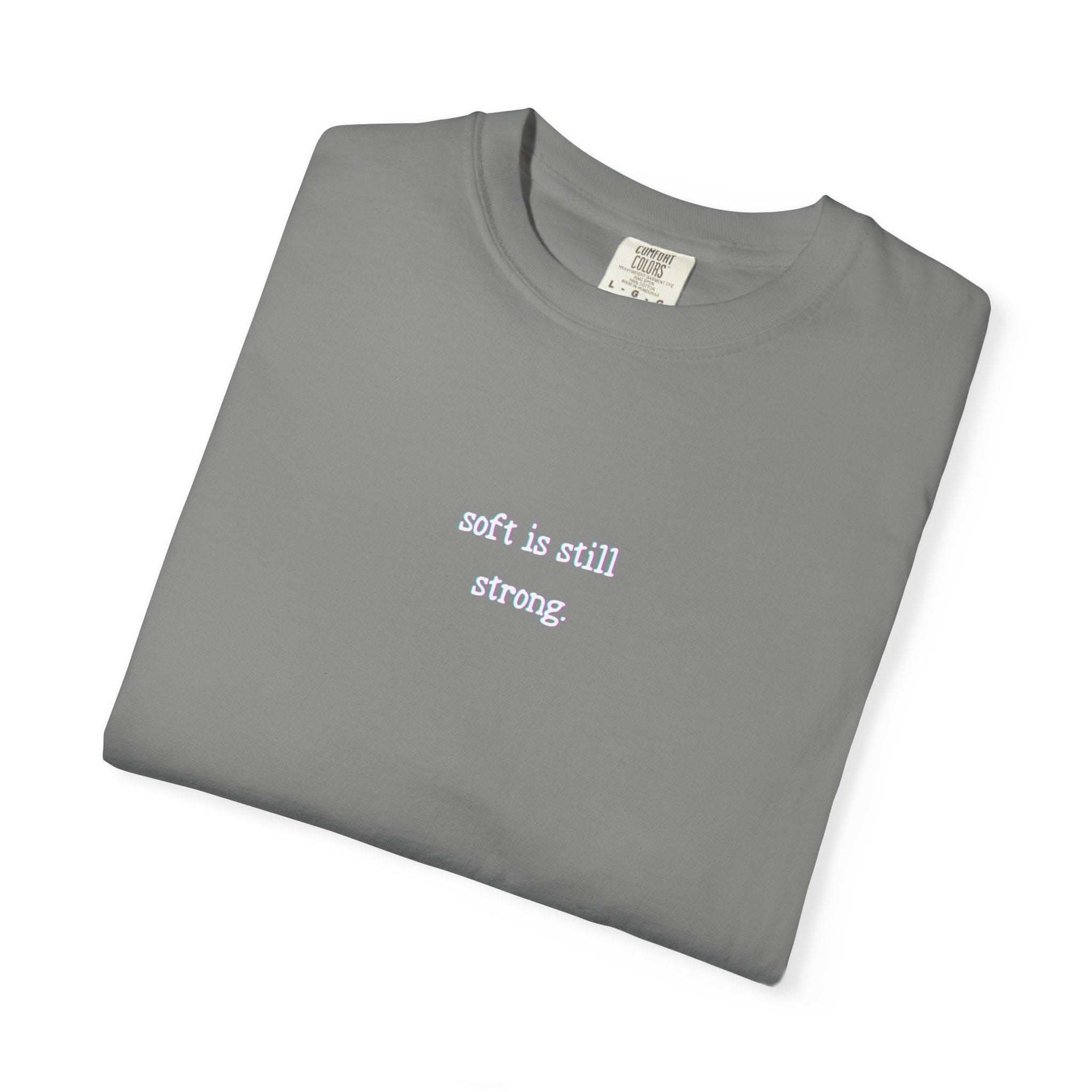 Folded gray t-shirt with 'soft is still strong' text on a white background