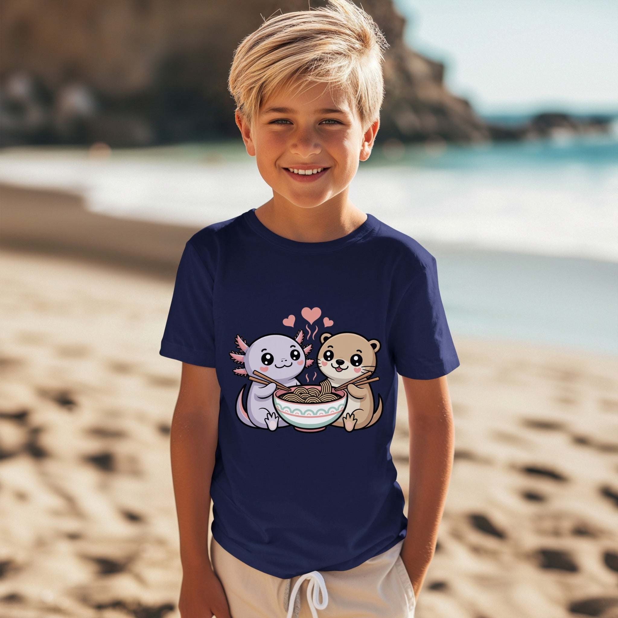 Child wearing navy youth tee with cute axolotl and otter holding a bowl of ramen design at the beach