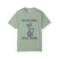 Flat lay of a bay green Comfort Colors 1717 t-shirt featuring a navy cat in a red party hat and “One Year Sober. Still Weird.” lettering.