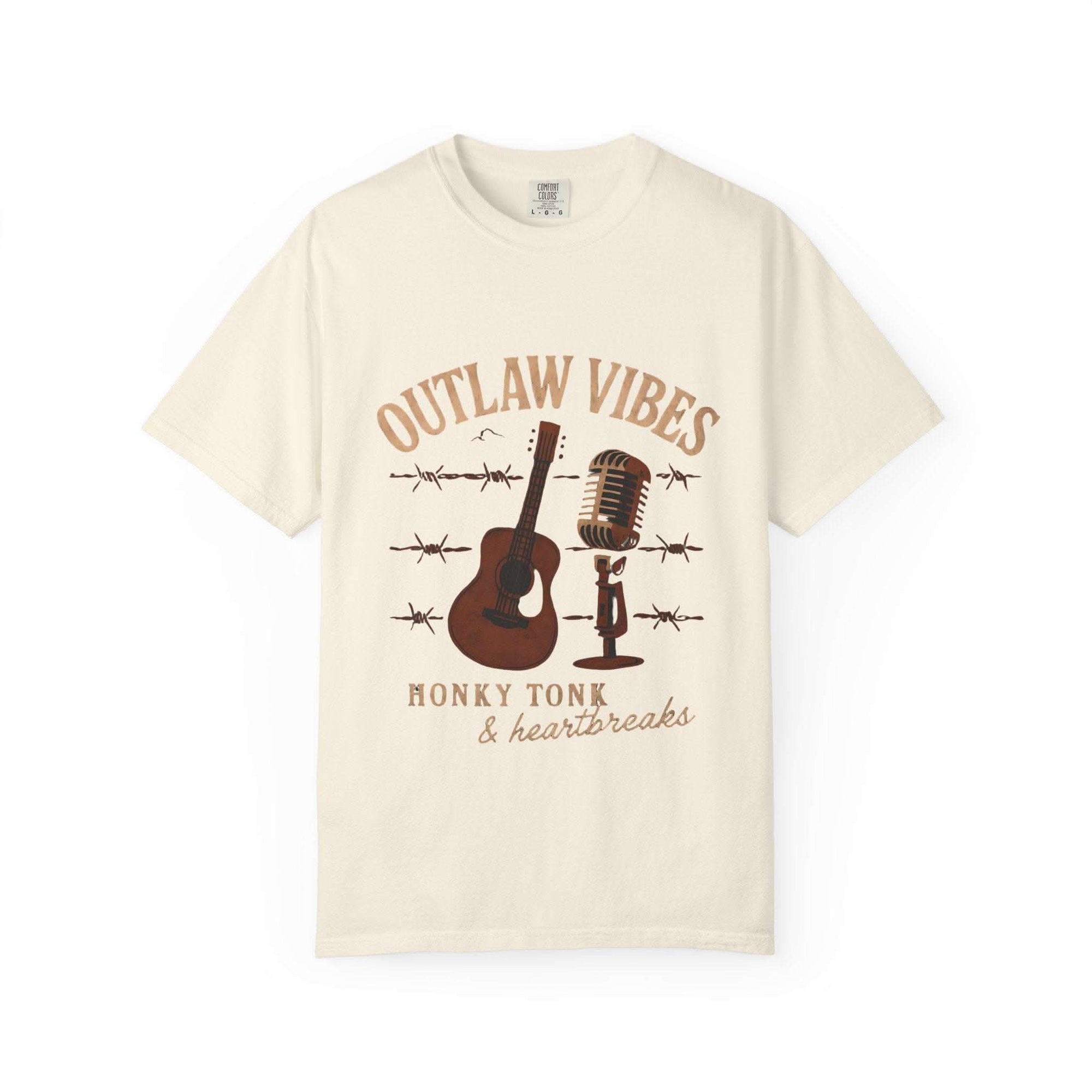 Beige t-shirt with 'Outlaw Vibes' graphic design featuring a guitar, microphone, and barbed wire on a white background.