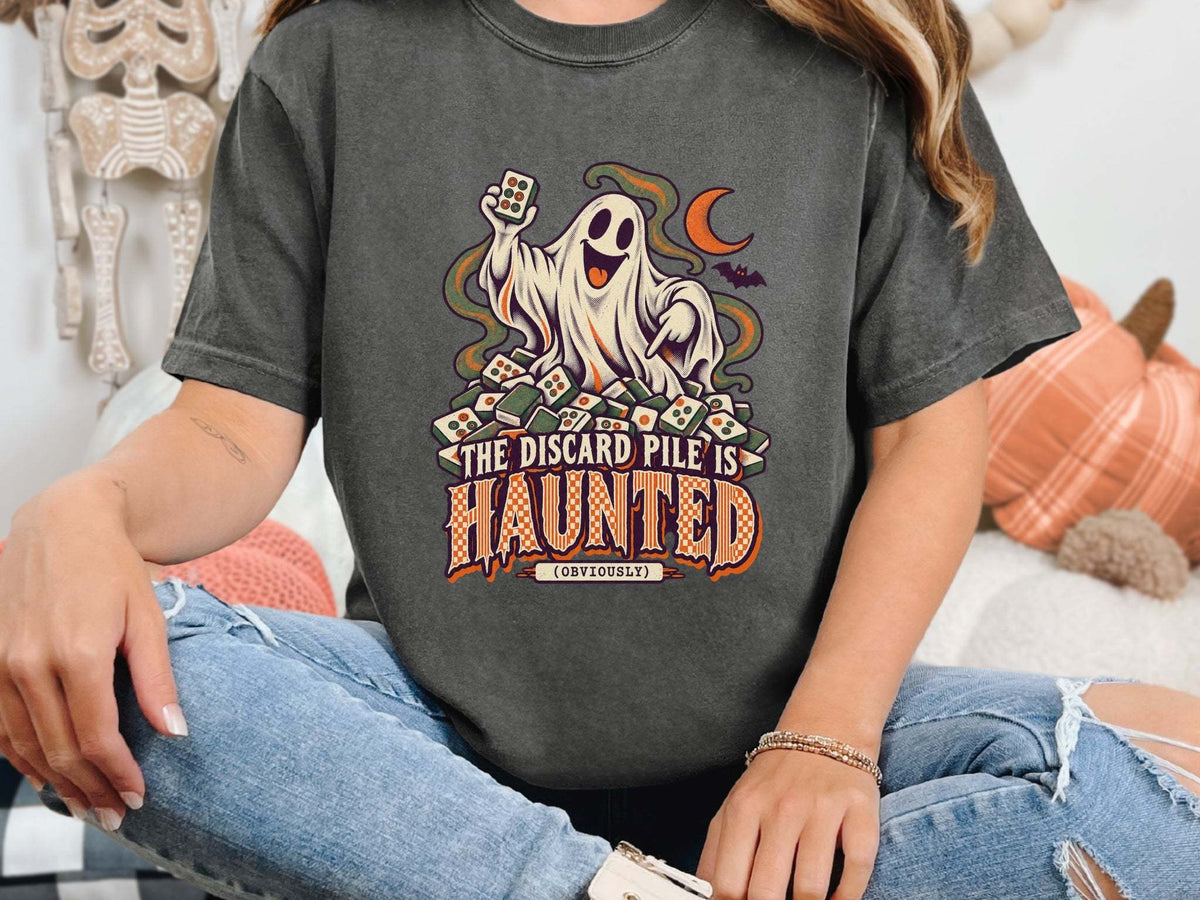Model wearing pepper Comfort Colors 1717 Halloween mahjong T-shirt with a ghost holding a tile and “The Discard Pile Is Haunted (Obviously)” lettering.