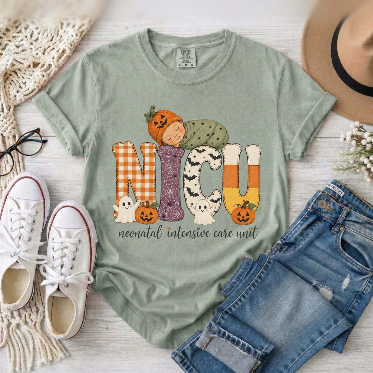 Bay green NICU nurse Halloween T-shirt with patchwork lettering, a sleeping baby in a pumpkin hat, ghosts, and jack-o’-lanterns.