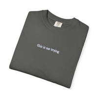 Folded dark gray t-shirt with 'this is me trying' text on a white background