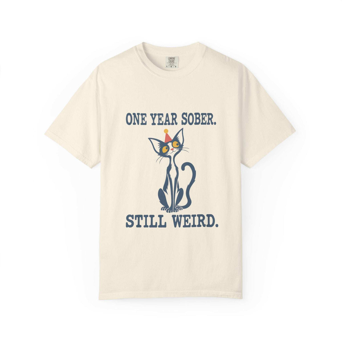 Flat lay of an ivory Comfort Colors 1717 t-shirt featuring a navy cat in a red party hat and “One Year Sober. Still Weird.” lettering.