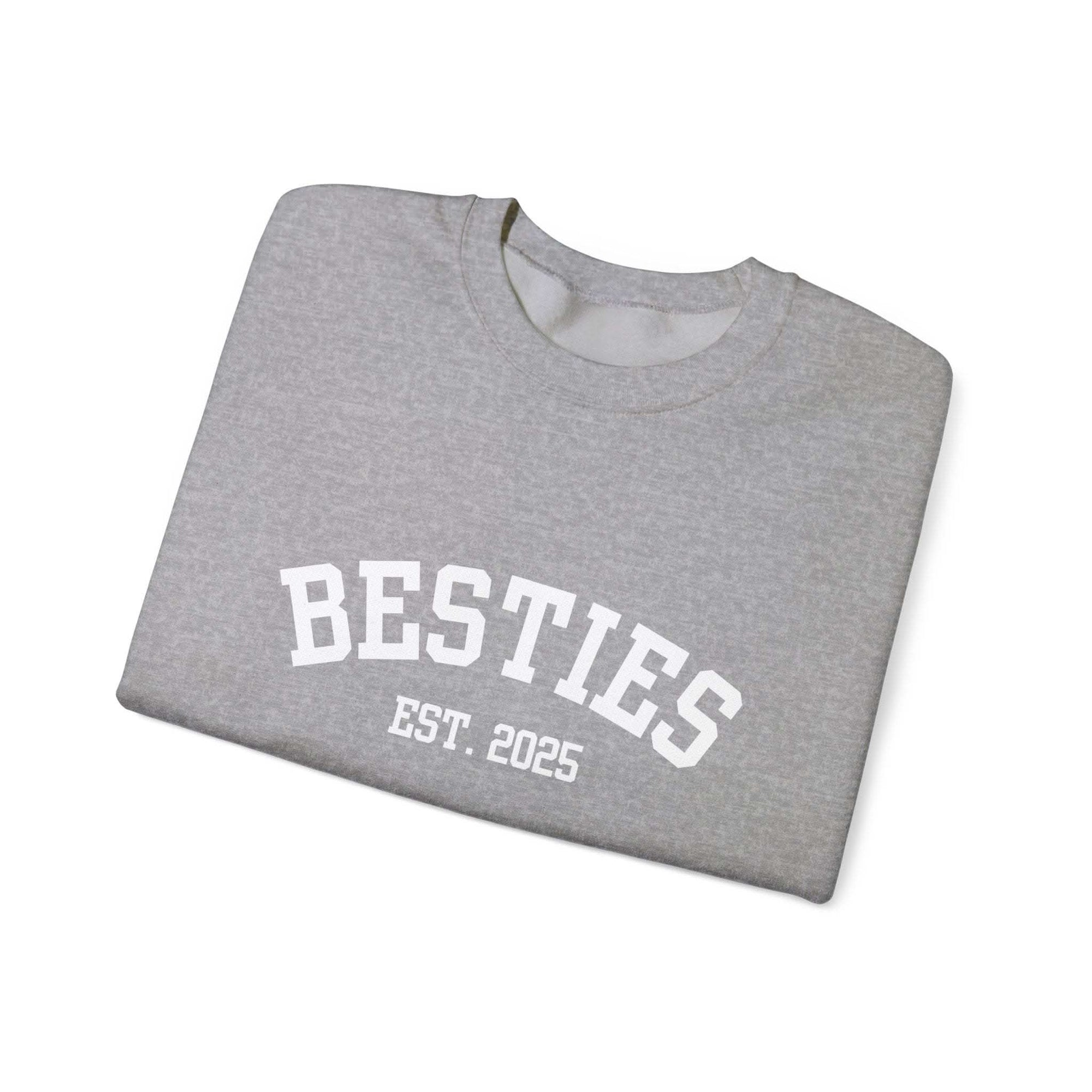 Folded gray sweatshirt with 'BESTIES EST. 2025' text on a white background
