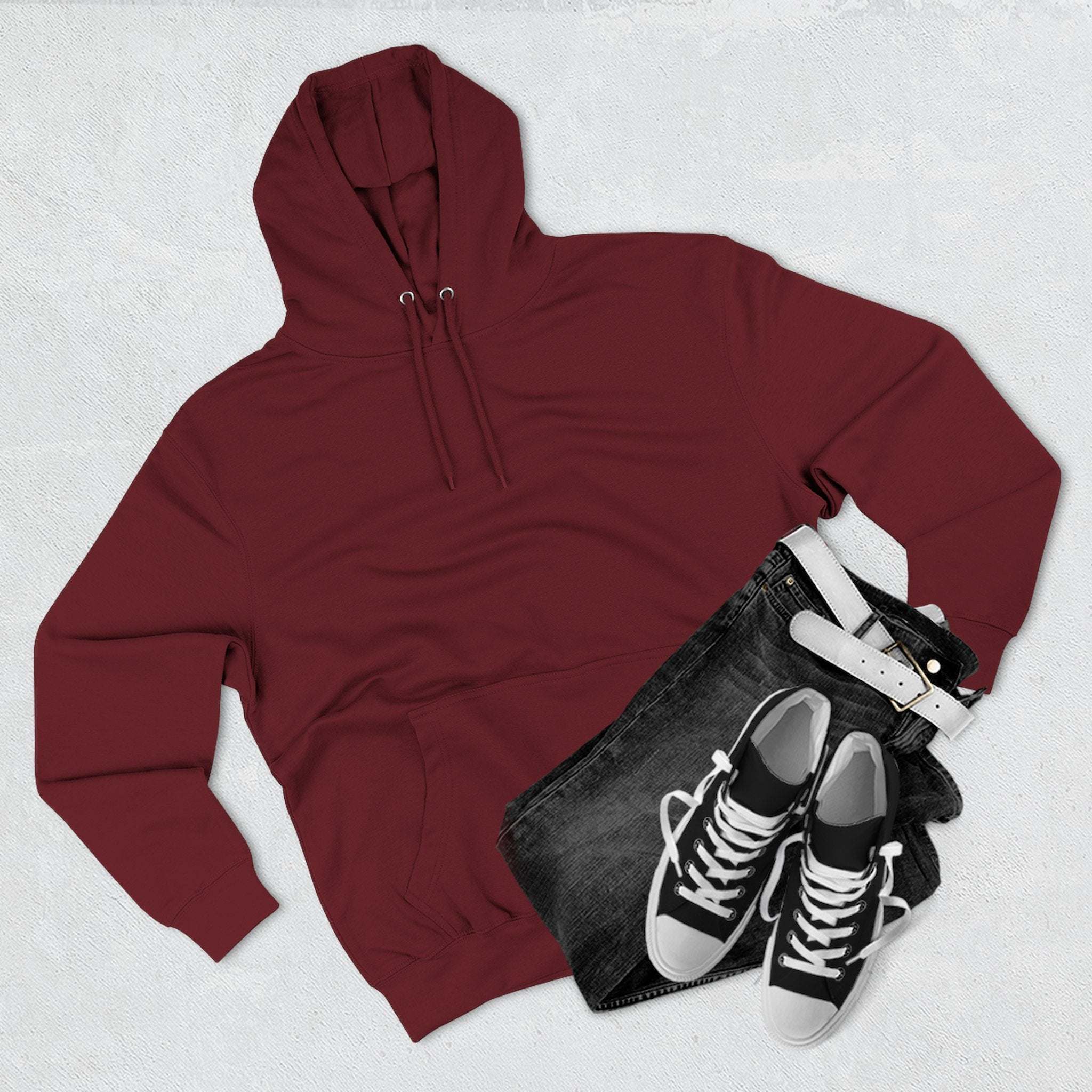 Maroon fleece hoodie with adjustable hood, kangaroo pocket, paired with black jeans and sneakers flat lay