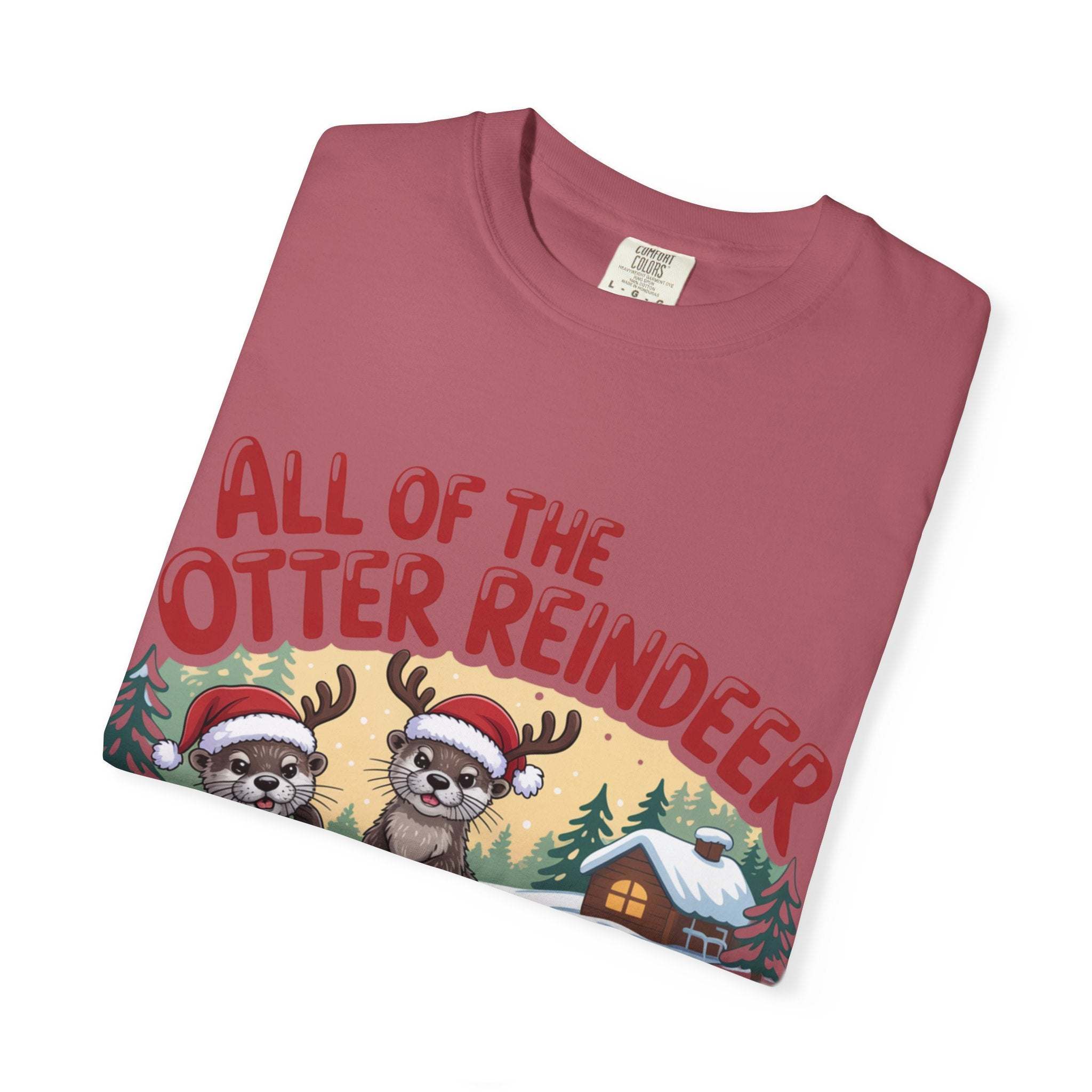 Folded dusty pink Otter Reindeer Tee with festive holiday design of otters in Santa hats and reindeer antlers.