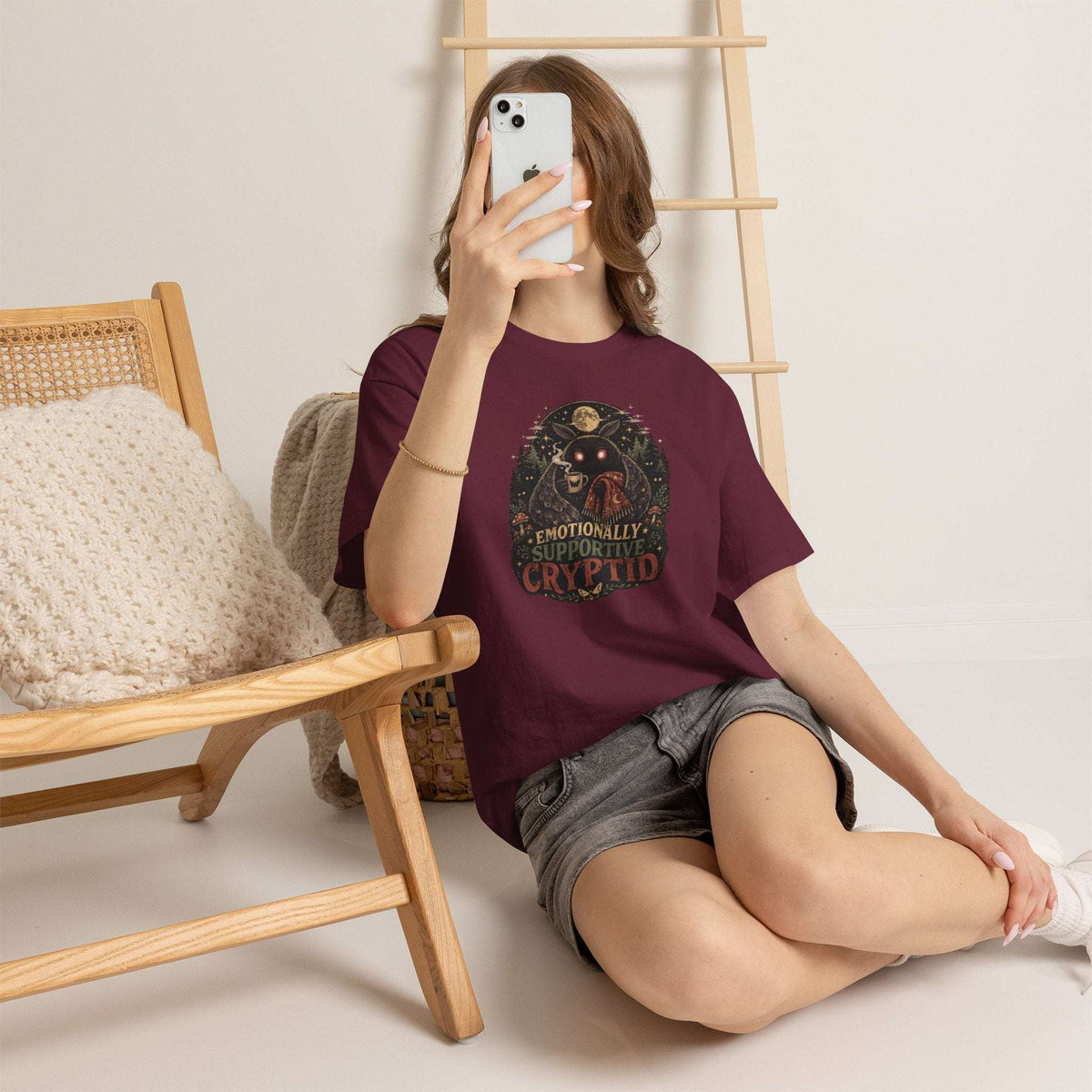 Surreal Mothman cryptid tee with glowing eyes holding coffee in cozy blanket under moonlit forest