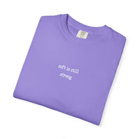 Folded purple t-shirt with 'soft is still strong' text on a white background