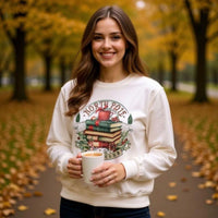 Woman wearing cozy Vintage North Pole Book Club sweatshirt holding a cup outdoors in autumn setting
