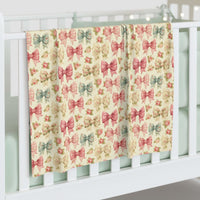Floral Coquette Bows swaddle blanket with pastel pink and blue bows hanging on white crib railing