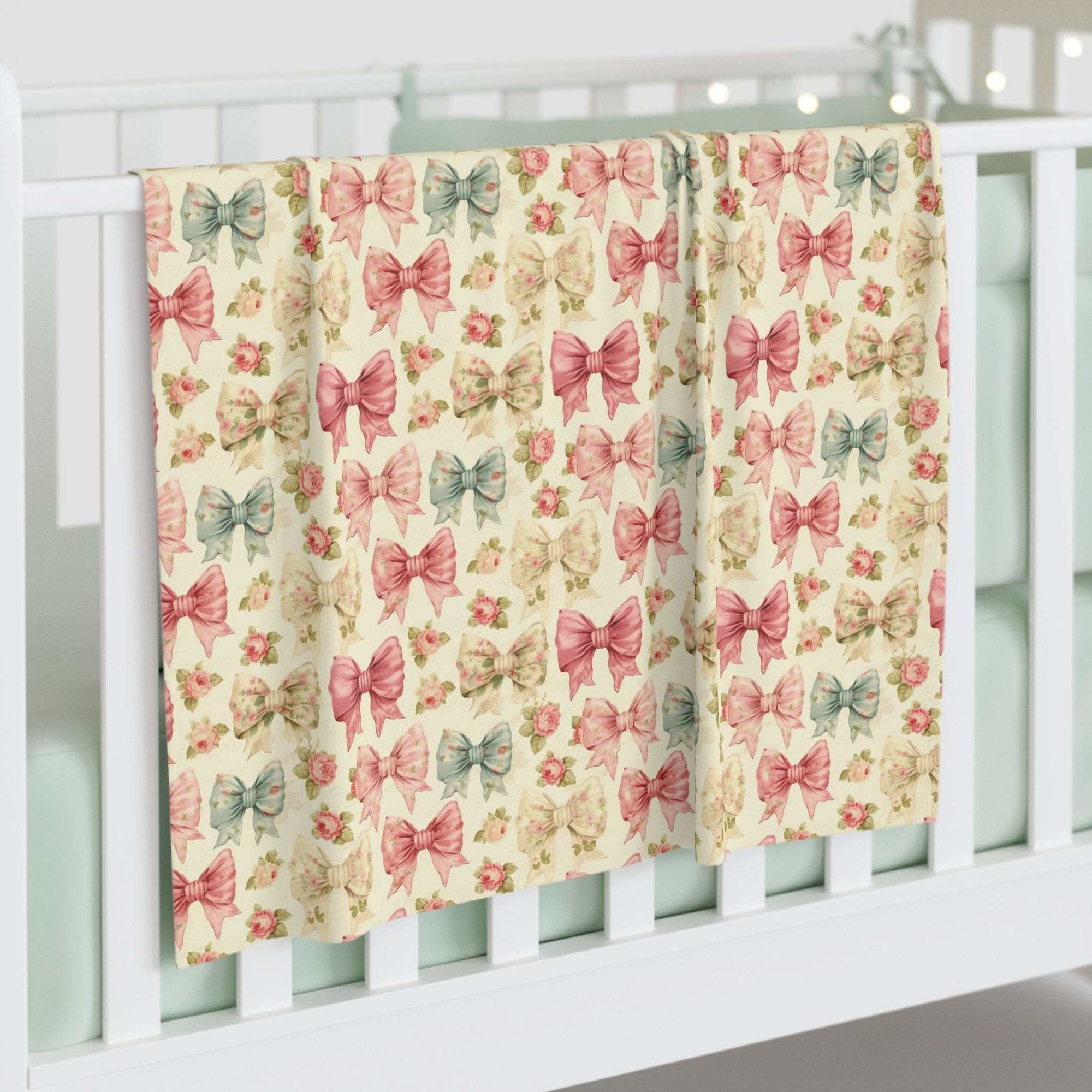 Floral Coquette Bows swaddle blanket with pastel pink and blue bows hanging on white crib railing
