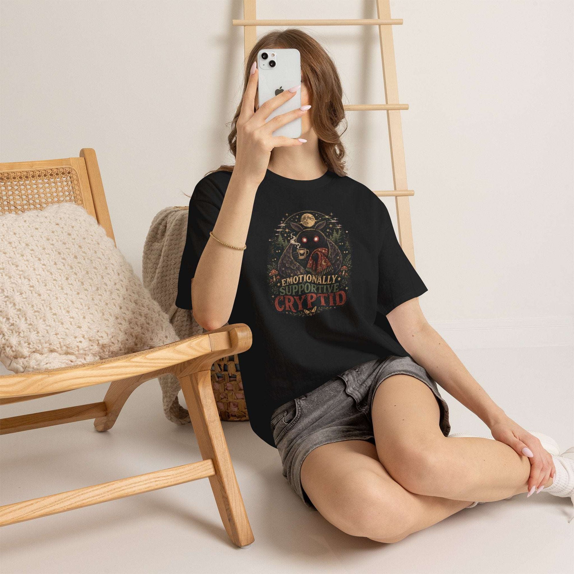 Surreal Mothman cryptid tee with glowing eyes holding coffee under moonlit forest canopy