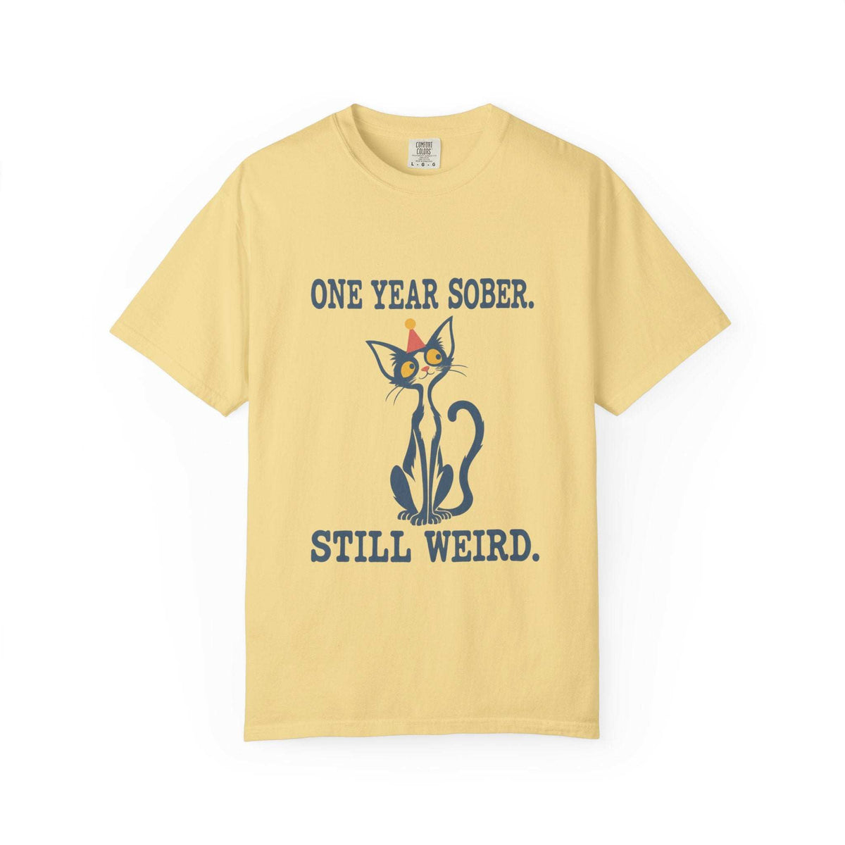Flat lay of an butter Comfort Colors 1717 t-shirt featuring a navy cat in a red party hat and “One Year Sober. Still Weird.” lettering.