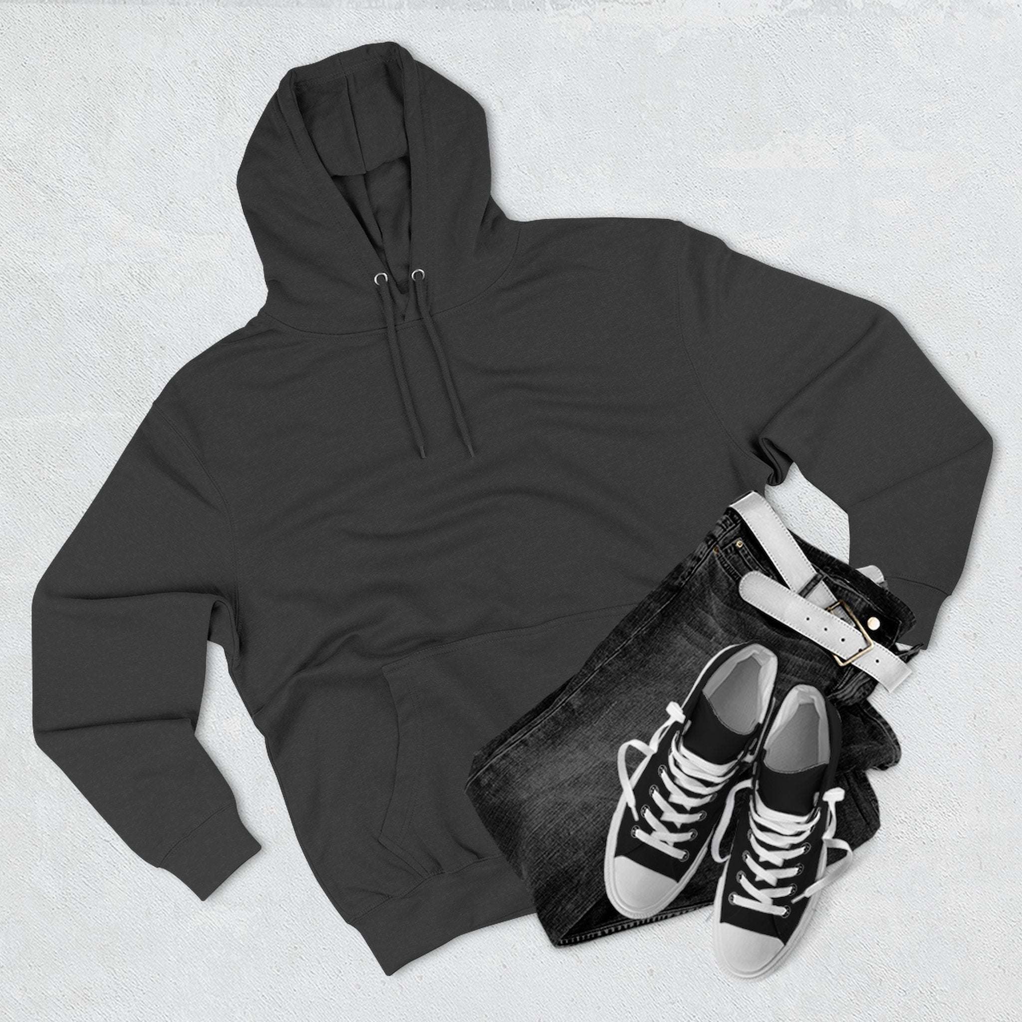Black fleece hoodie with adjustable hood, paired with black jeans and sneakers laid flat on a light surface