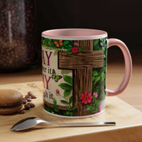 Mug with floral and cross design on a wooden surface with coffee beans and a spoon.